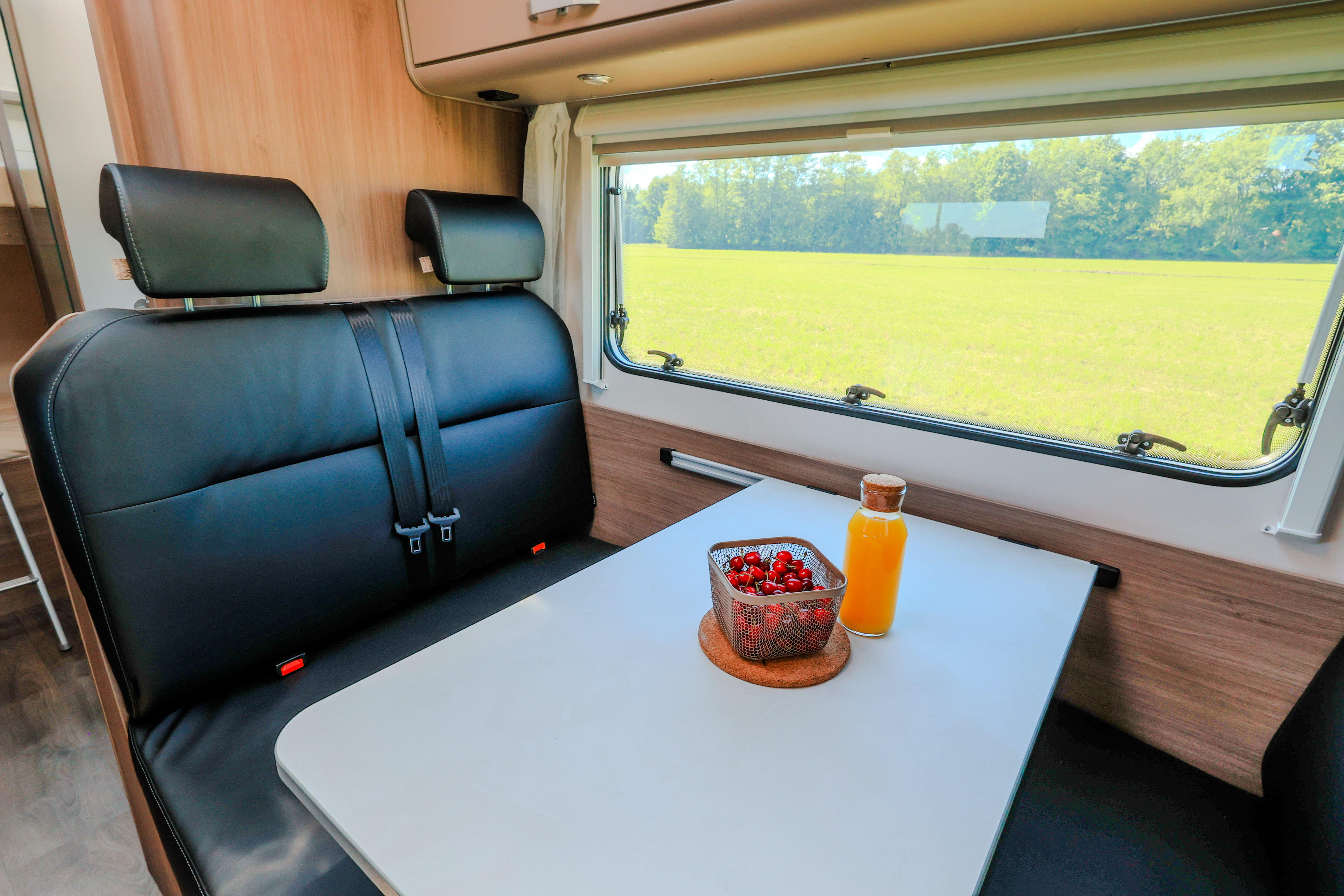 Van interior with black leather seats, dining table, bottle of juice, bowl of cherries, window on the side.