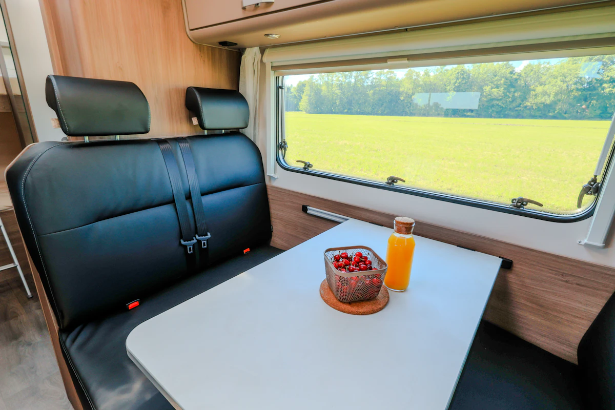 Van interior with black leather seats, dining table, bottle of juice, bowl of cherries, window on the side.