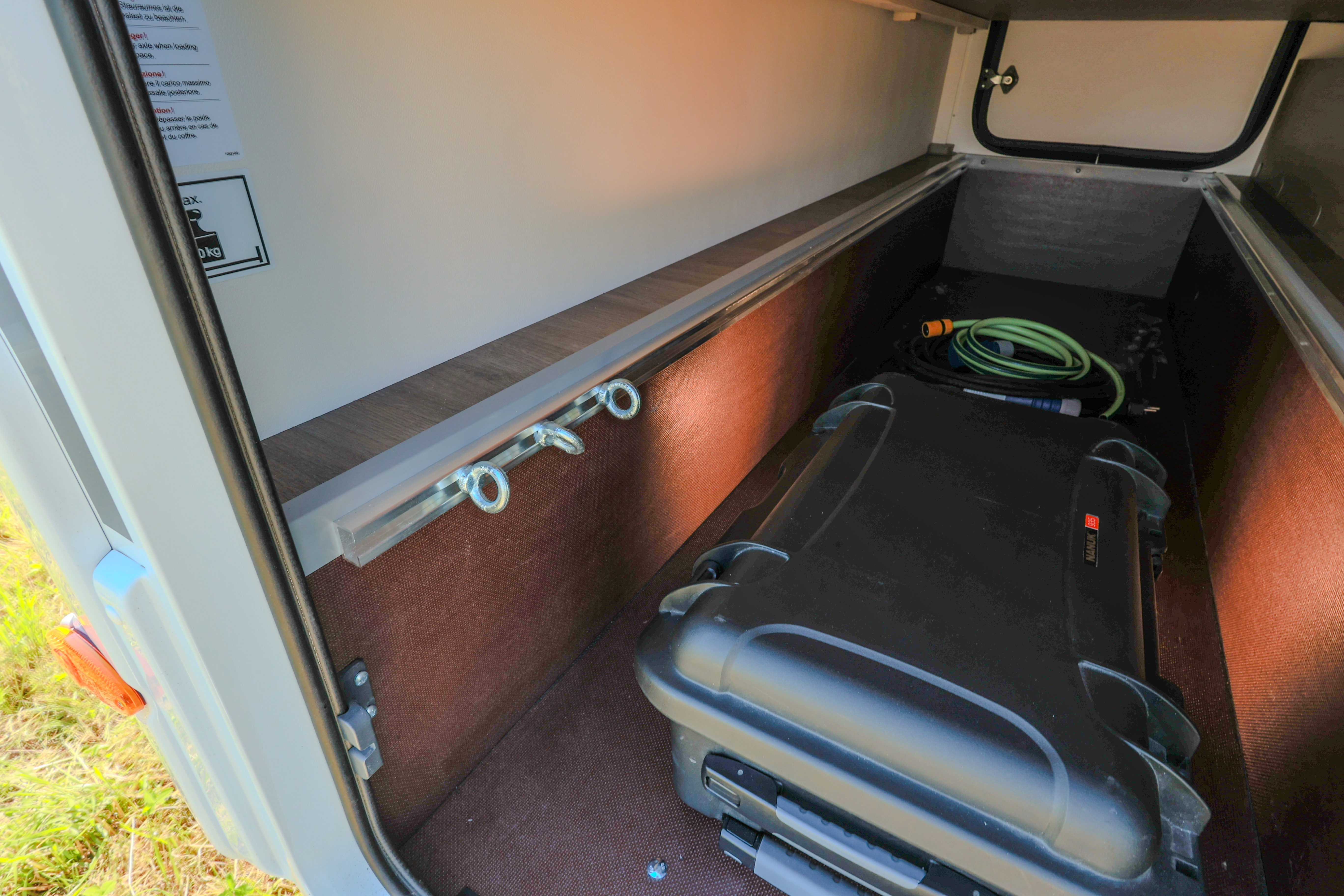 Van interior storage compartment with shelves, hooks, suitcase, and a coiled hose visible inside.