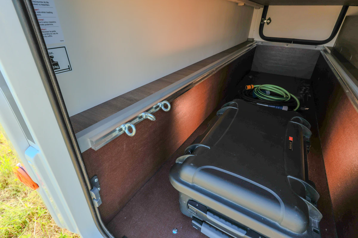 Van interior storage compartment with shelves, hooks, suitcase, and a coiled hose visible inside.