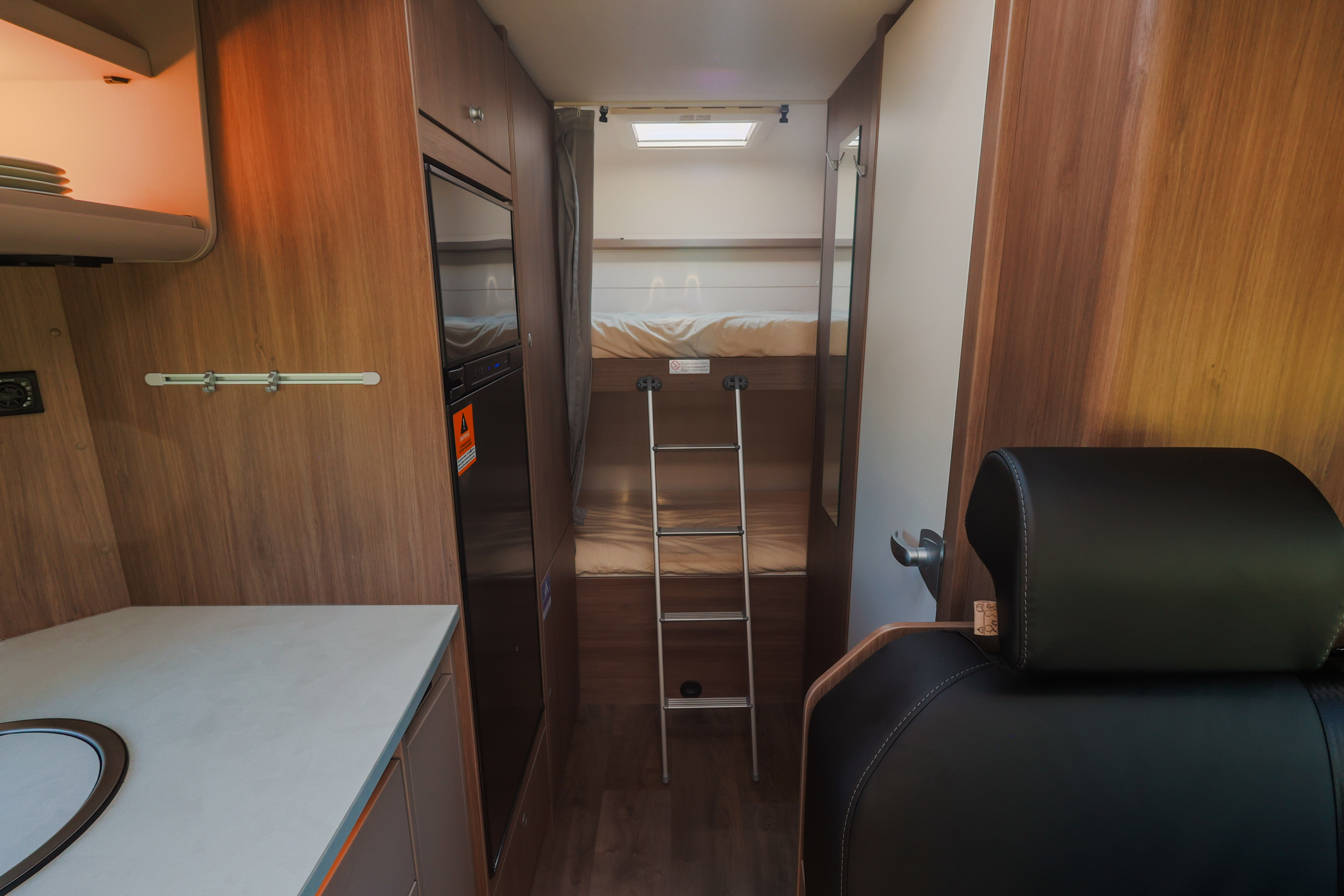 Camper van interior with kitchen counter, storage cabinets, and rear sleeping area accessible by ladder.