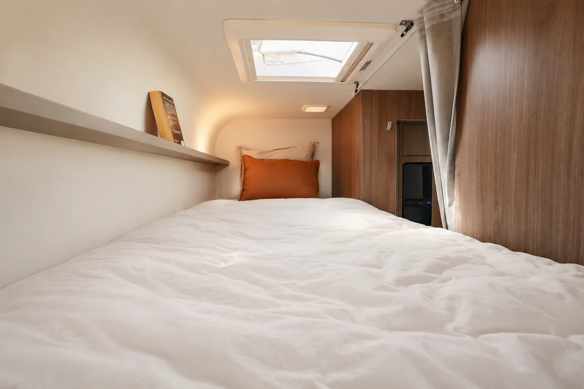 Van interior with bed, skylight, shelf, cushion, wood paneling, and curtain visible.