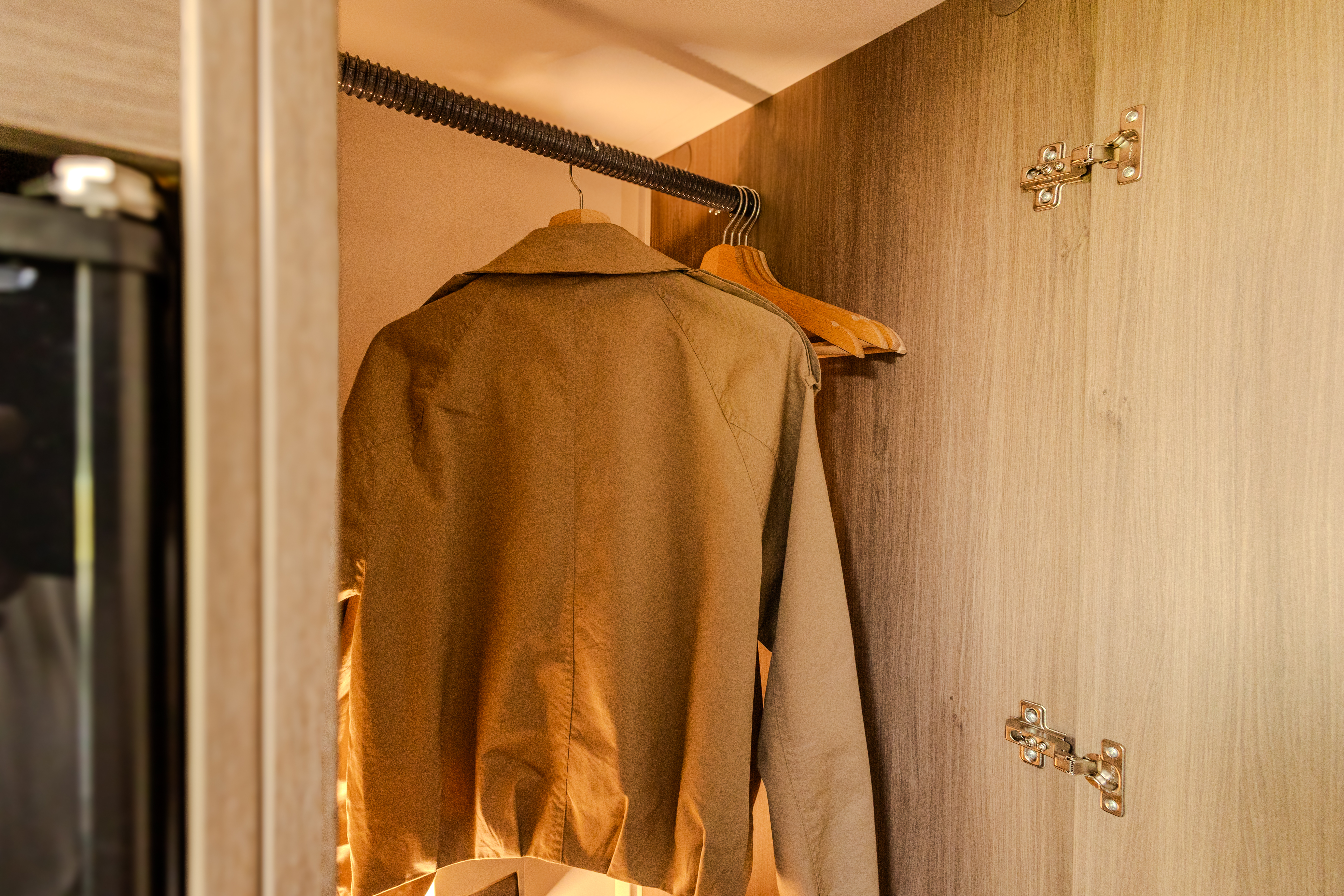 Wooden wardrobe inside van with clothes hanging on rail and hinges visible on the door.