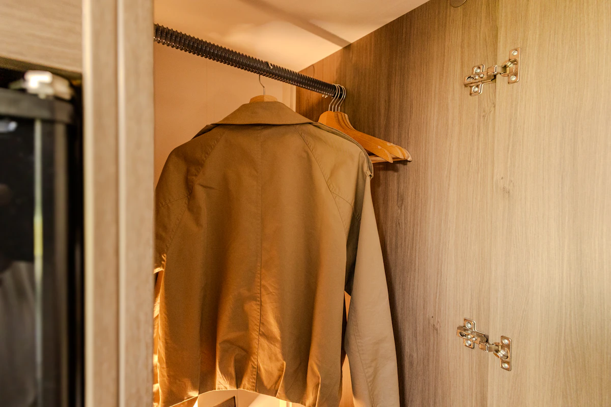 Wooden wardrobe inside van with clothes hanging on rail and hinges visible on the door.