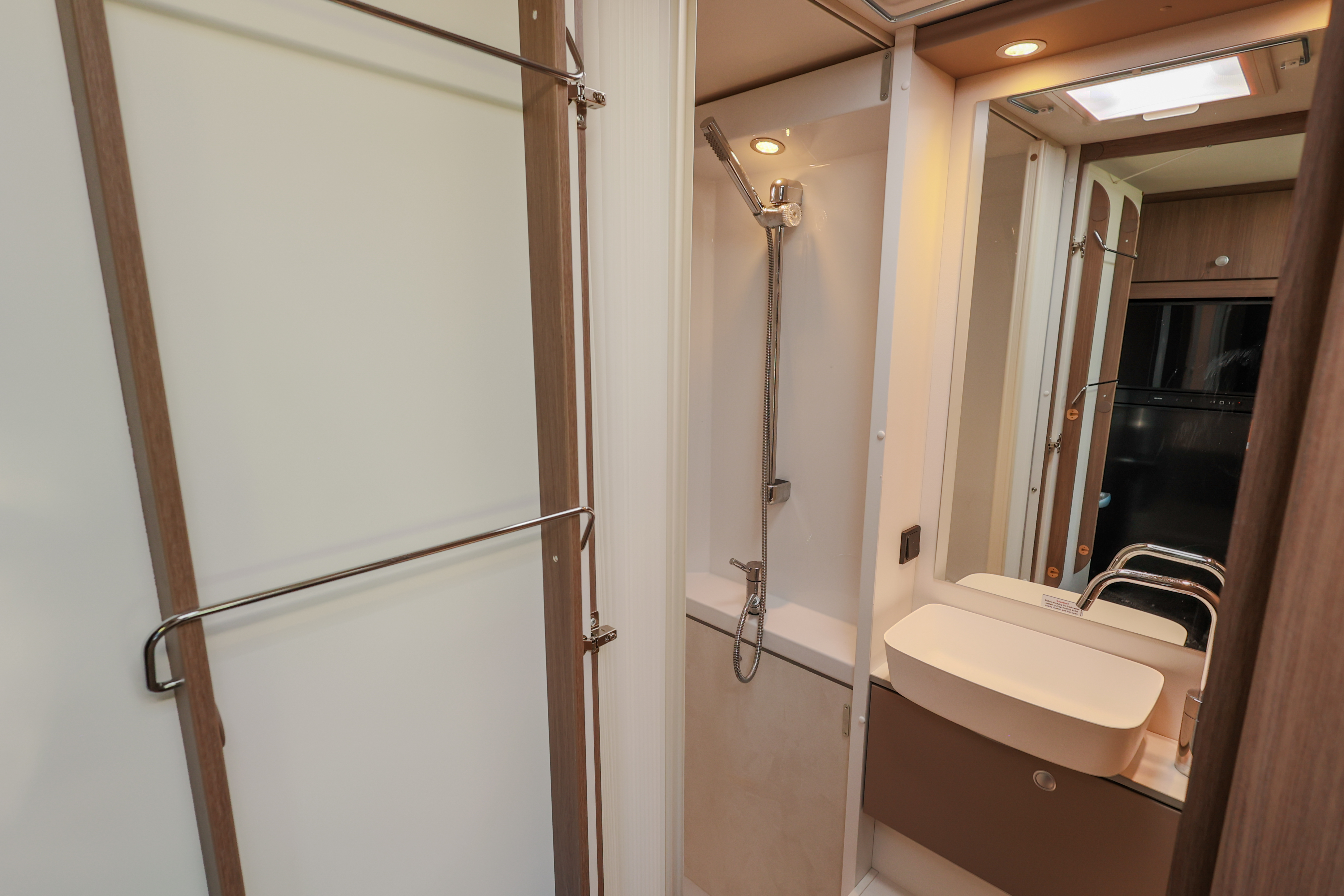 Van bathroom interior with shower, sink, mirrored cabinet, and towel rack visible.