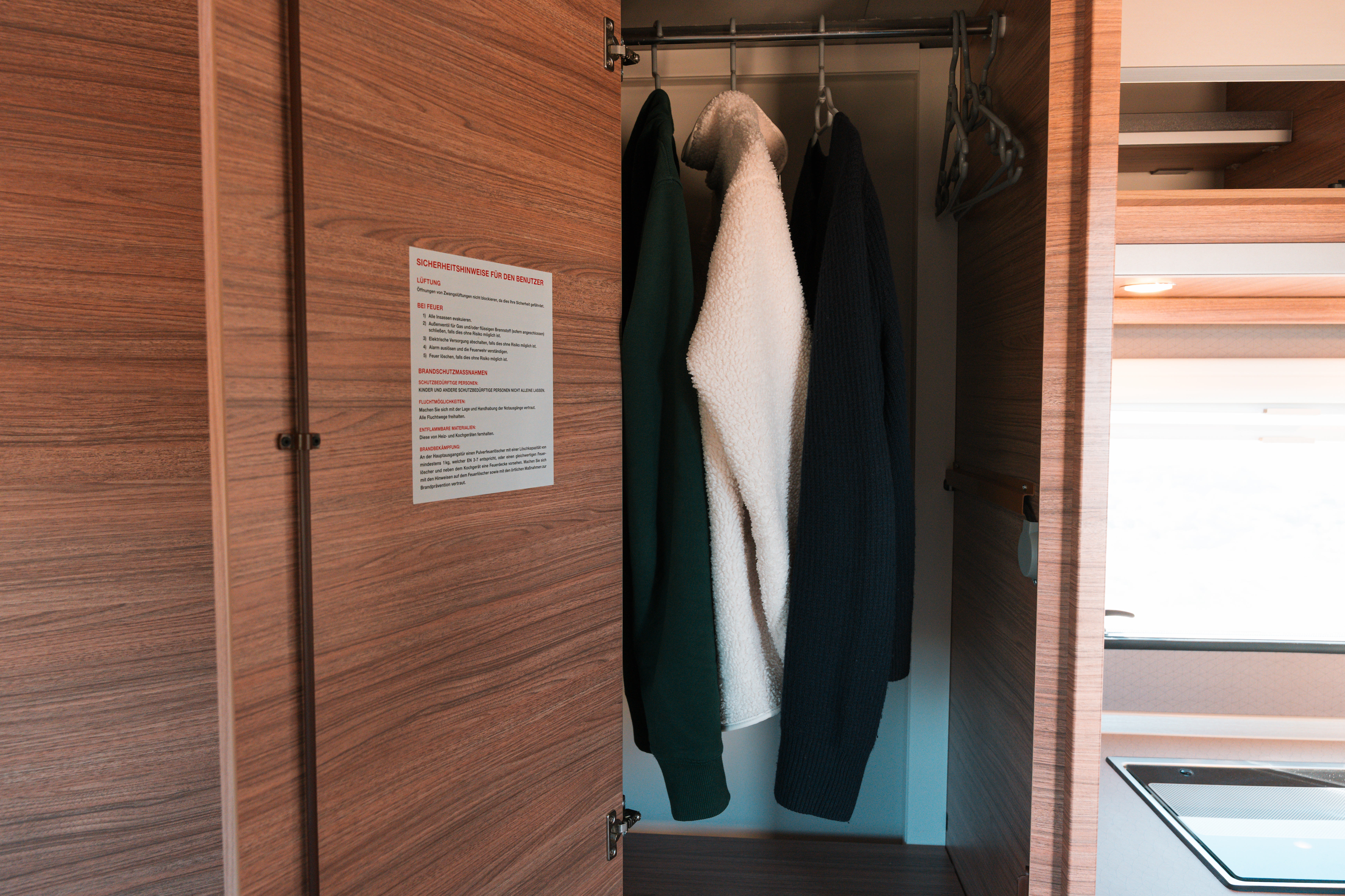 Wardrobe inside van with hanging clothes, wooden doors, and interior shelving visible.