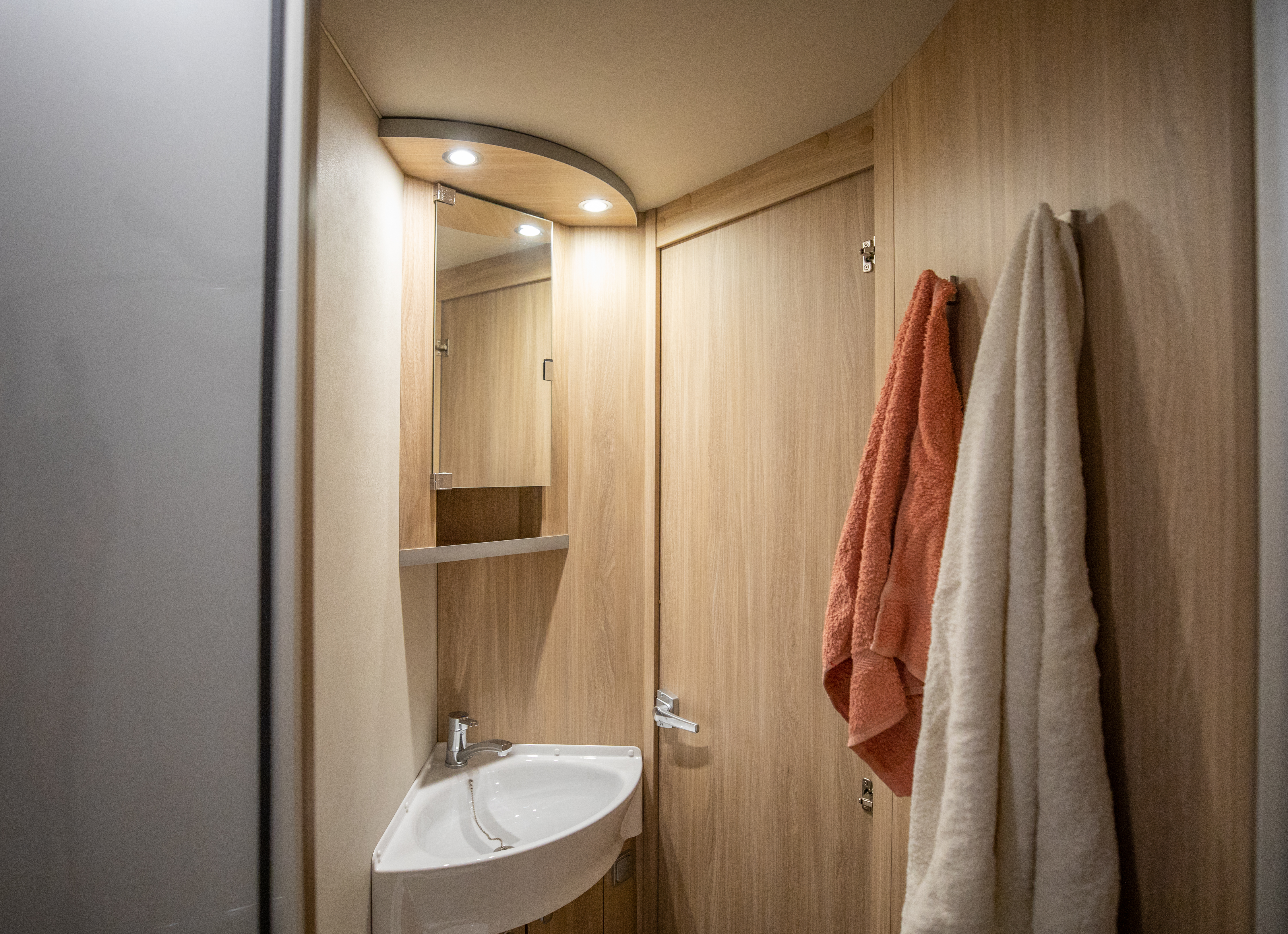 Van bathroom interior with sink, mirror, wooden cabinets, door, and two towels hanging on the wall.