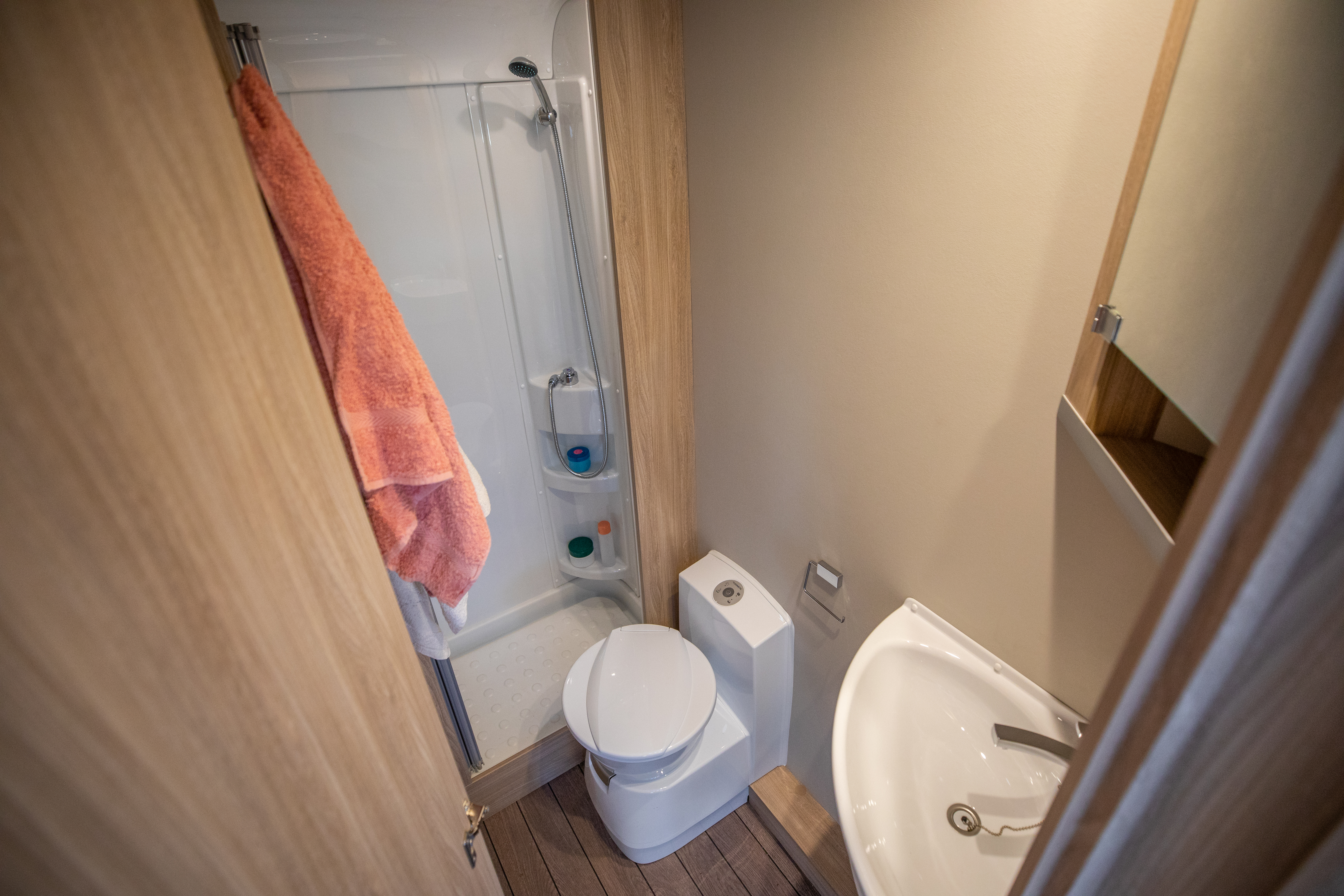 Compact camper van bathroom with toilet, sink, mirror cabinet, towel rack, and enclosed shower visible.