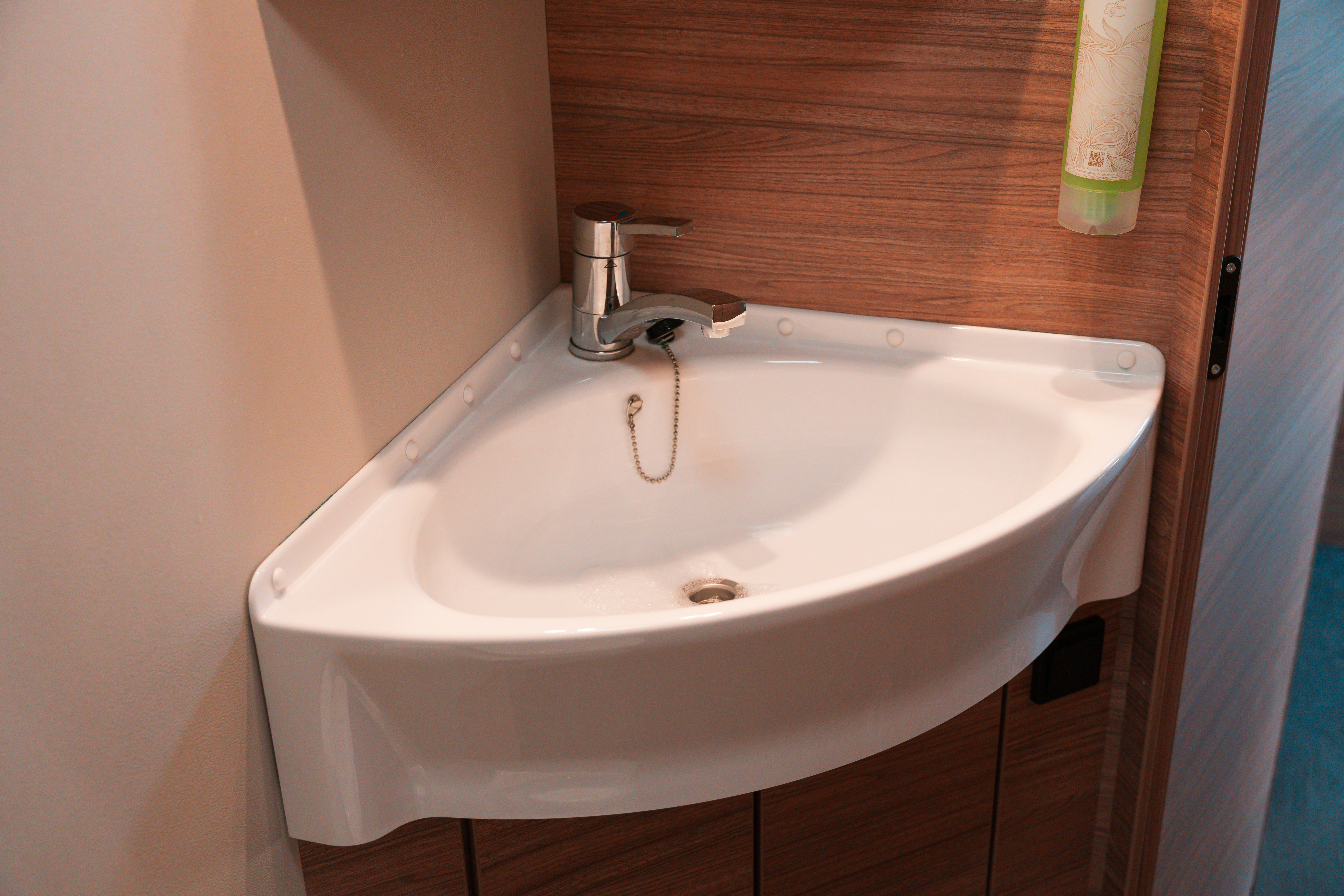 Corner sink with faucet and wood panel background inside van bathroom.