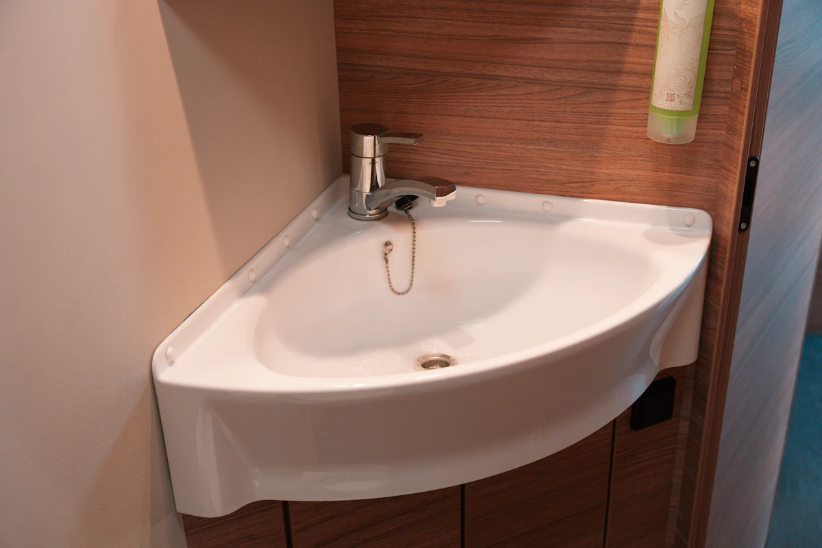Corner sink with faucet and wood panel background inside van bathroom.