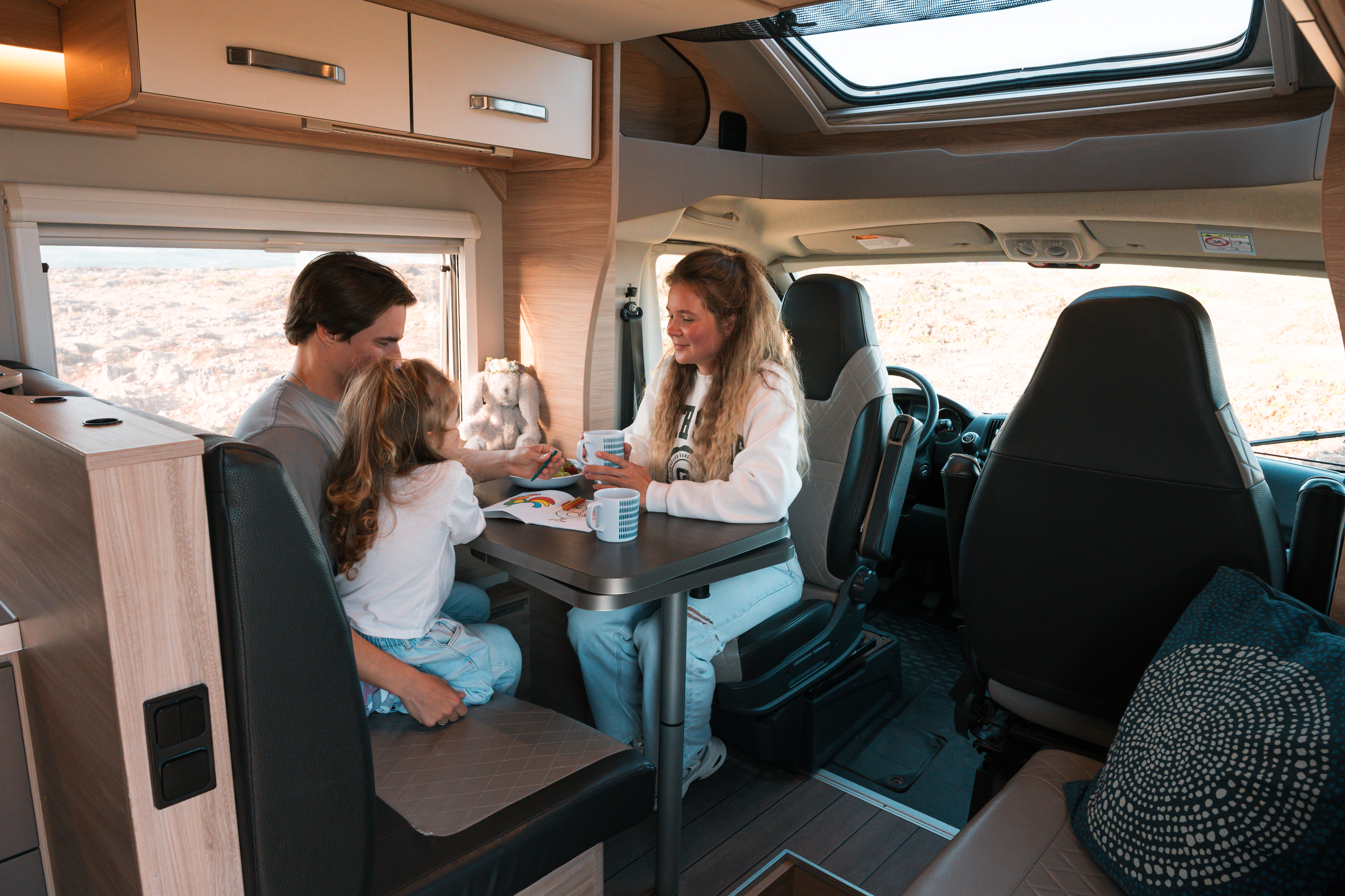 Van interior with dining table, bench seat, swivel front seats, overhead cabinets, window, and skylight visible.