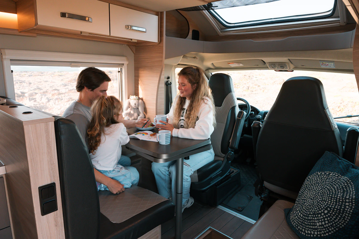 Van interior with dining table, bench seat, swivel front seats, overhead cabinets, window, and skylight visible.