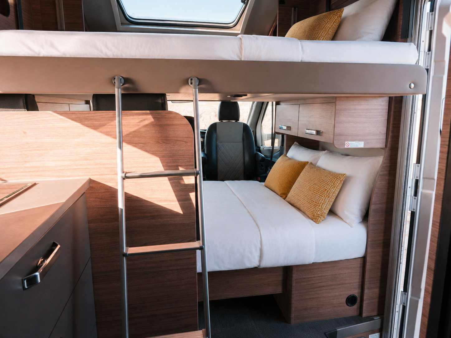 Van interior with bunk beds, ladder, kitchen counter, wooden cabinets, and seating area visible.