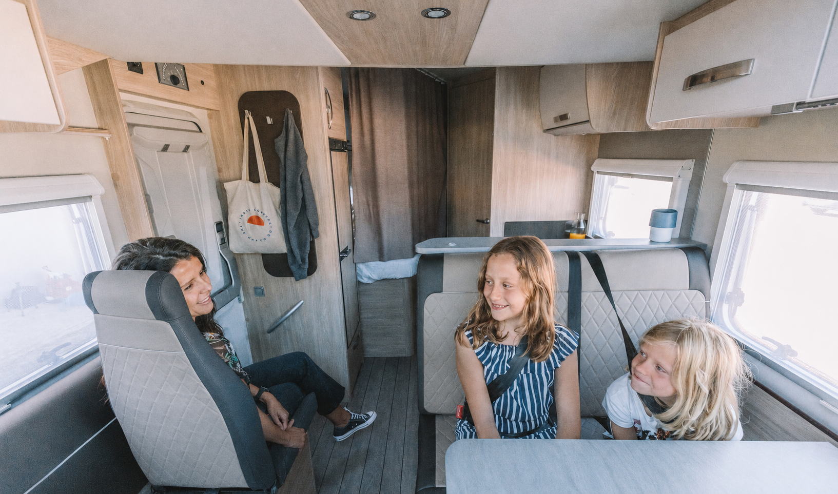 Van interior with seating area, dining table, overhead cabinets, and rear kitchen visible.