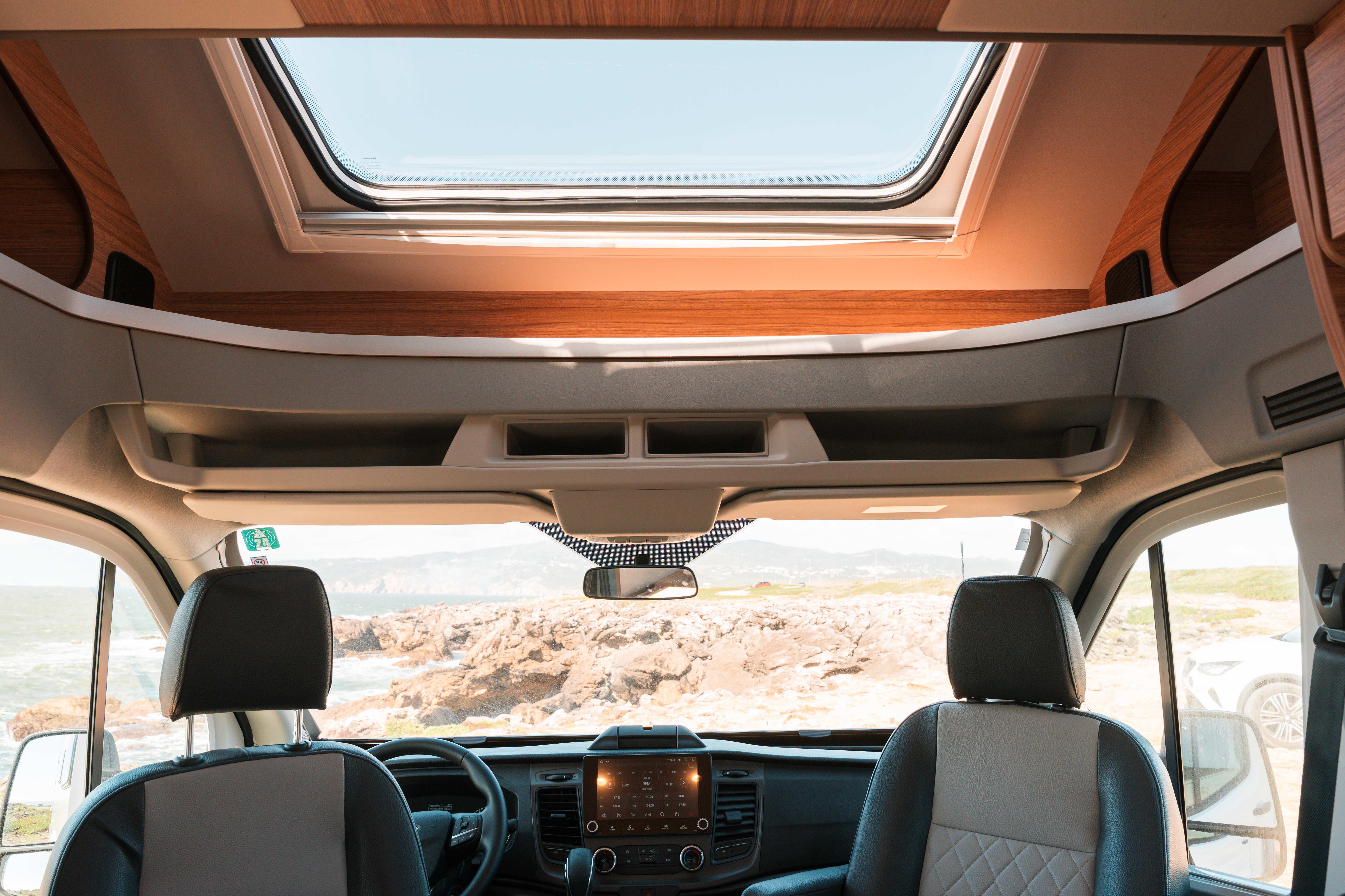 Van interior with two front seats, dashboard, overhead storage, and large skylight above driver's area.