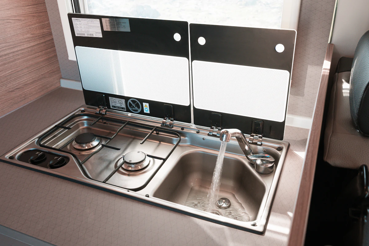 Compact van kitchen with two-burner stove, sink, running water, and glass covers in countertop layout.