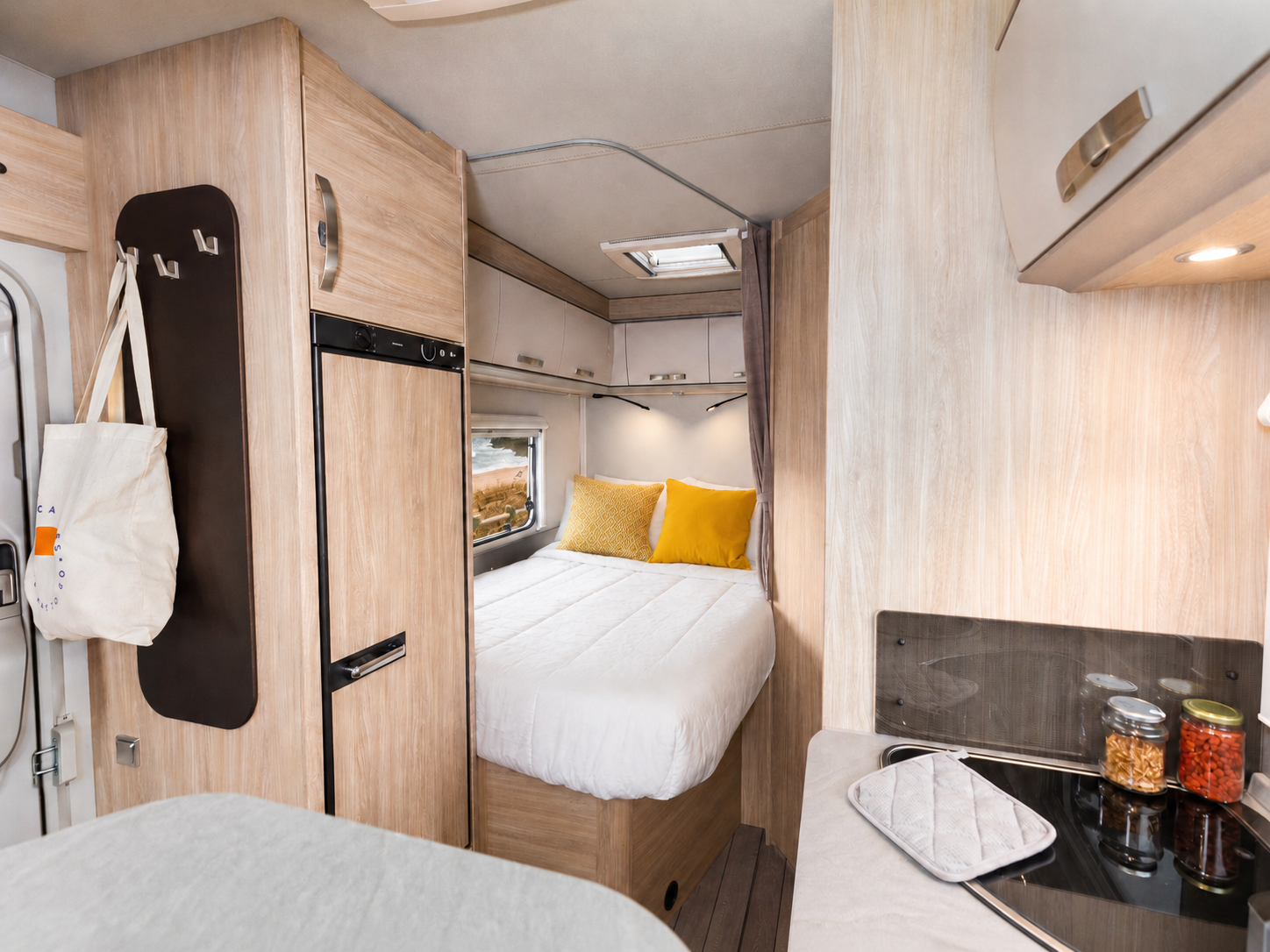Van interior with a rear bed, kitchen area, overhead cabinets, and compact fridge visible.