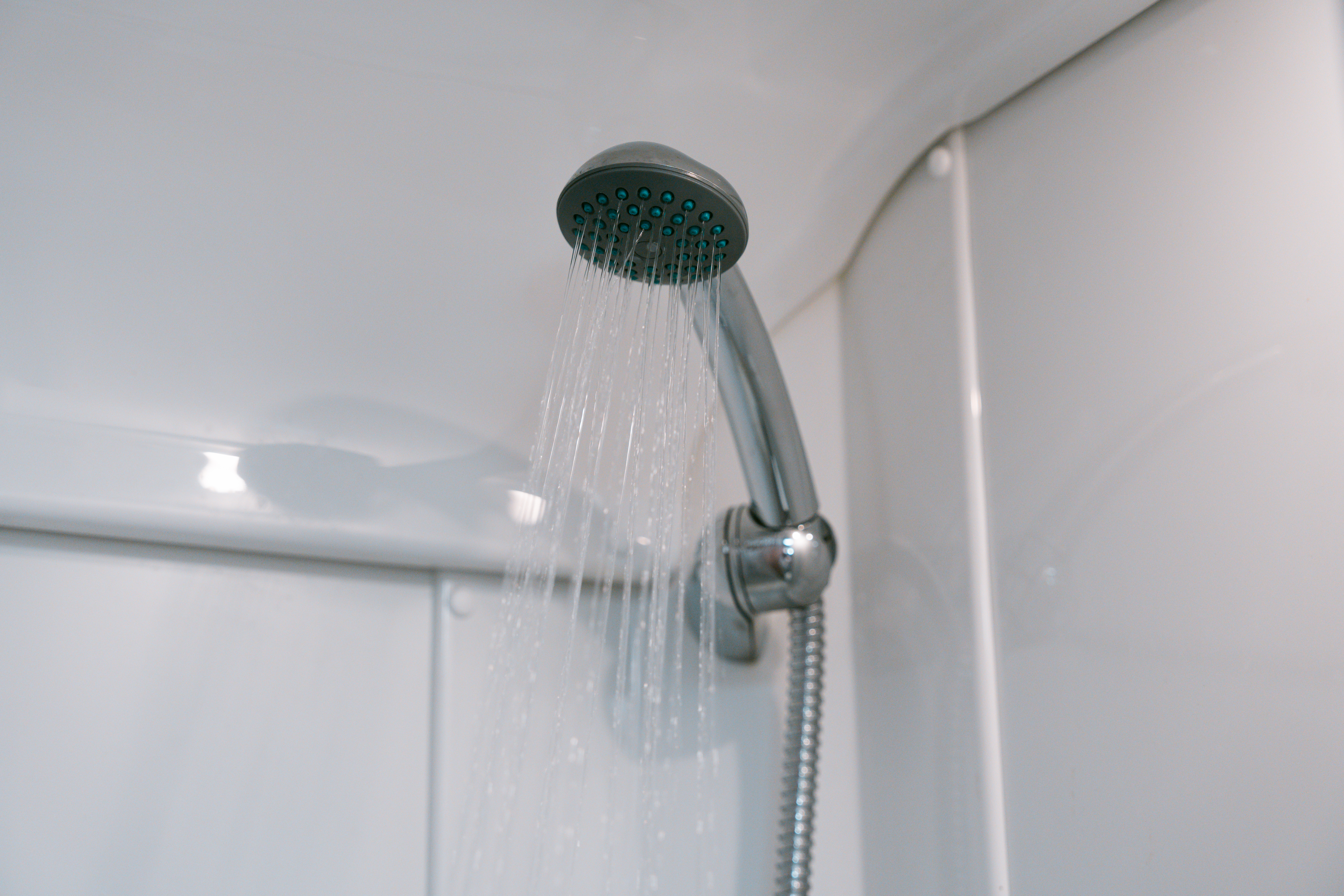 Showerhead with running water in a van bathroom, silver fixtures, white walls and curved ceiling visible.