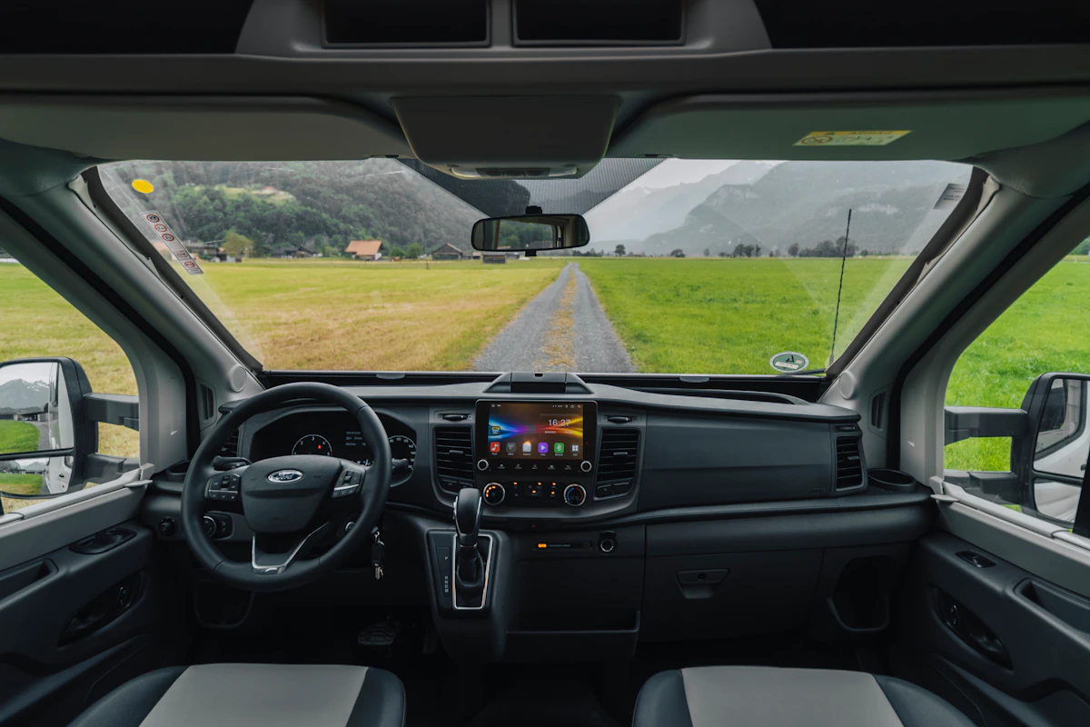Van interior showing front seats, dashboard with touchscreen, steering wheel, and gear lever, viewed from inside.