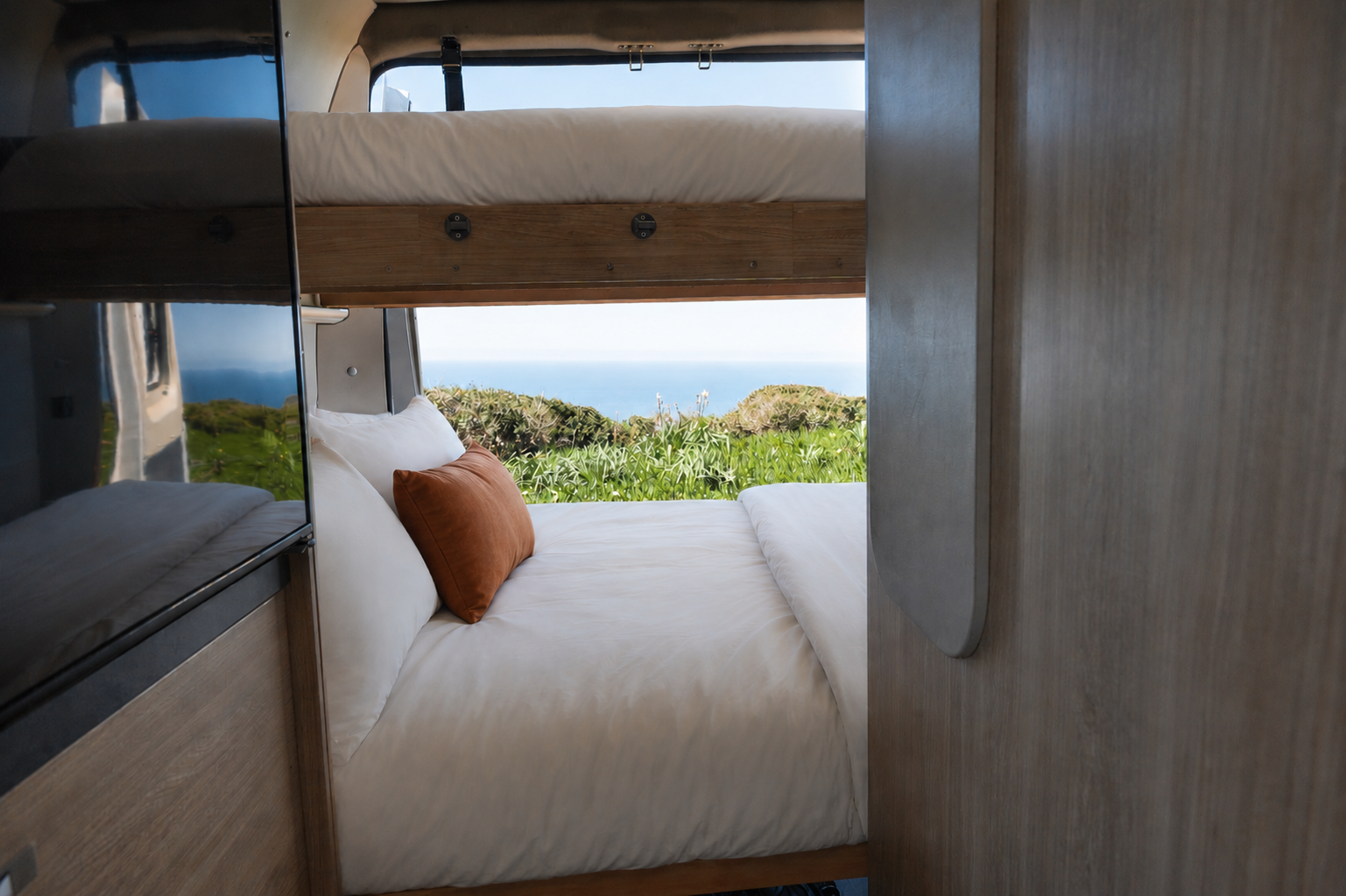 Van interior with bunk beds, pillows, wood cabinets, and window at the rear.