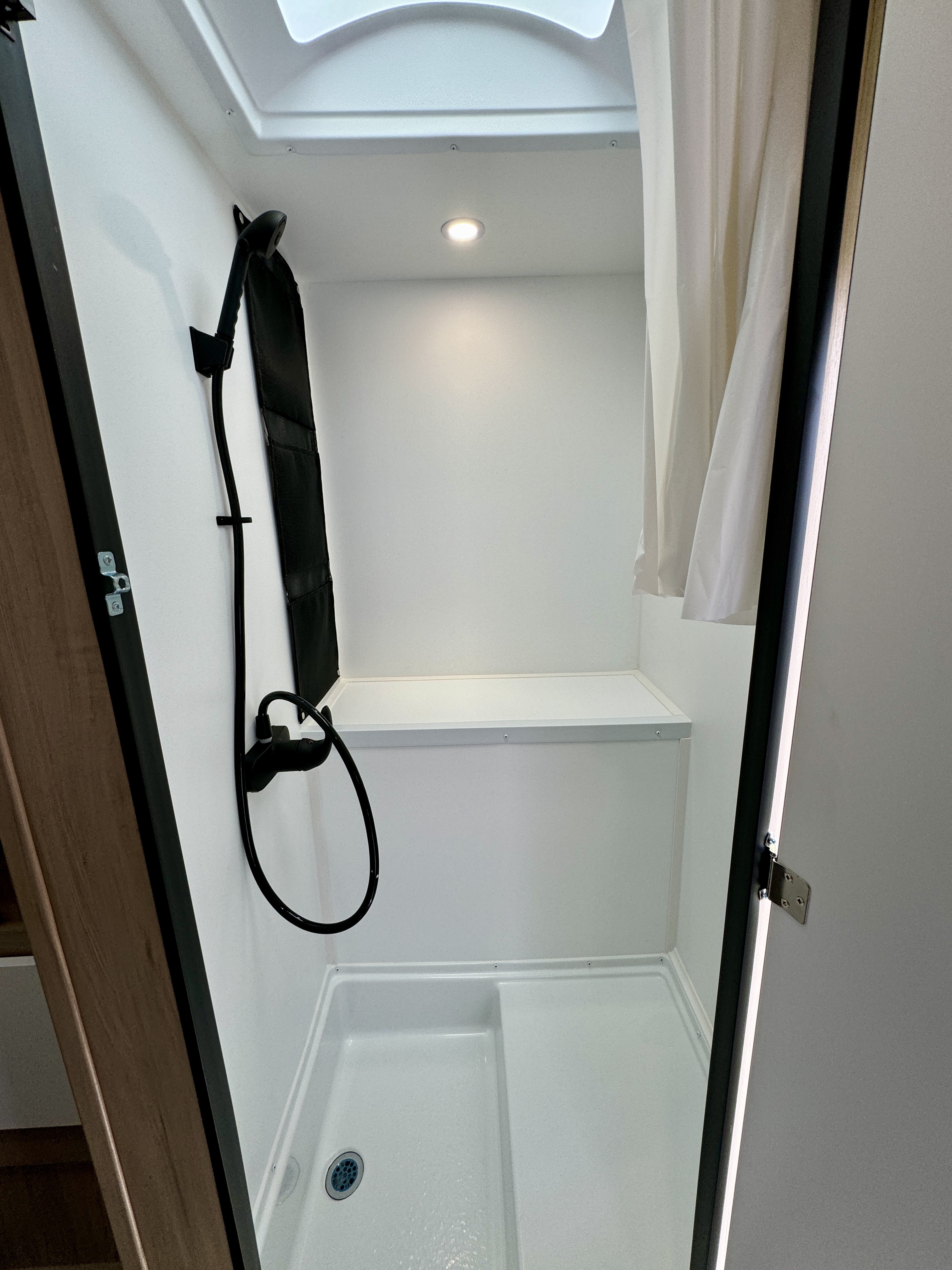 Van interior with shower area, wall-mounted showerhead, white walls, ceiling light, and partial curtain visible.