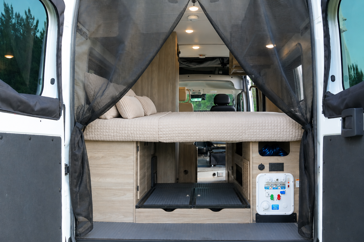 Rear interior view of van with raised bed, storage compartments, and utility panel visible.