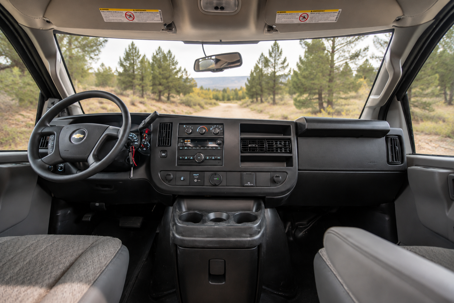 View of van front cab interior showing dashboard, steering wheel, two seats, and center console with cup holders.