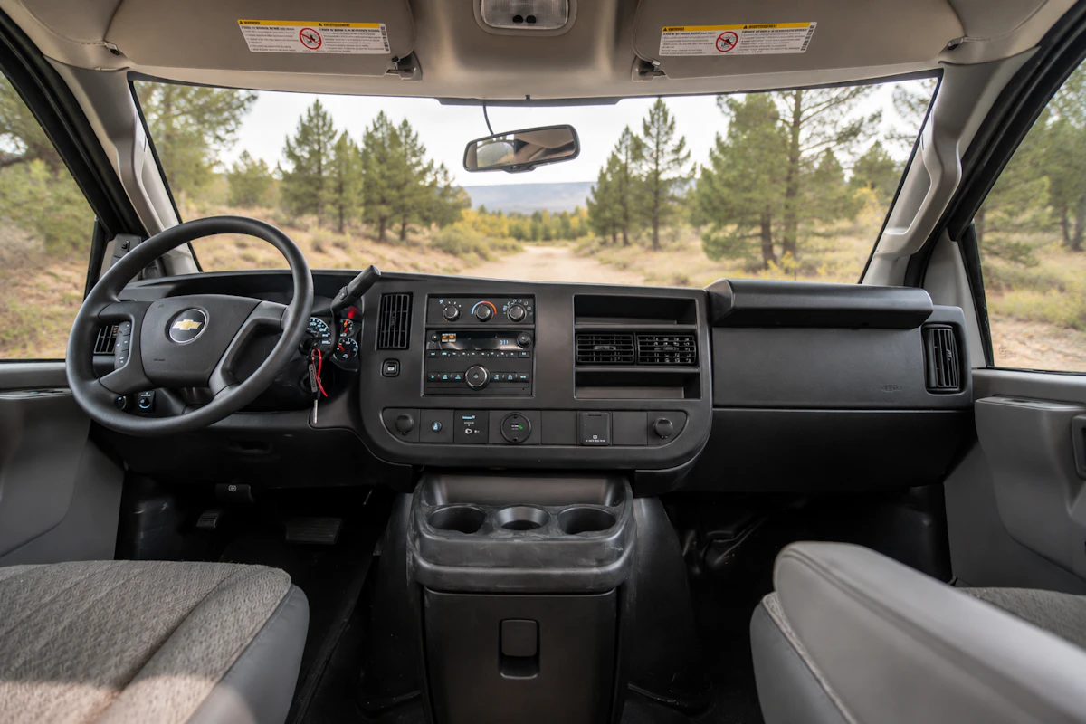View of van front cab interior showing dashboard, steering wheel, two seats, and center console with cup holders.