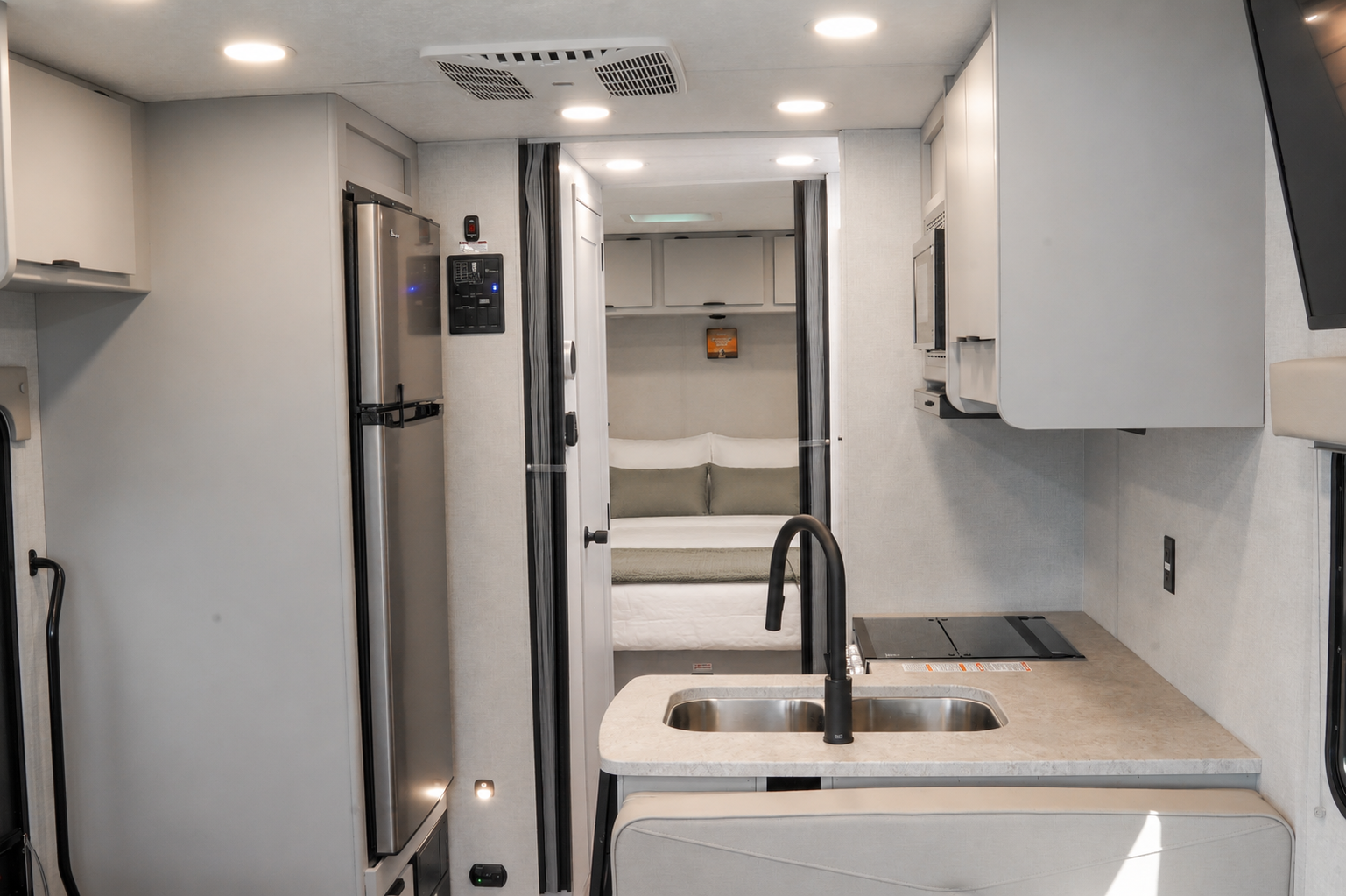 Kitchen with sink, countertop, cabinets, fridge, and rear sleeping area visible inside the camper van.