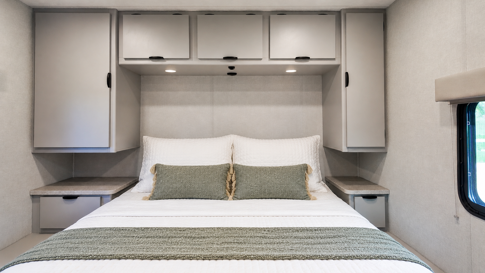 Van interior with double bed, overhead cabinets, side wardrobes, and two small bedside tables.