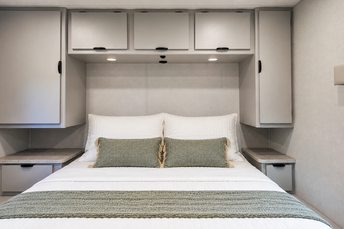 Van interior with double bed, overhead cabinets, side wardrobes, and two small bedside tables.