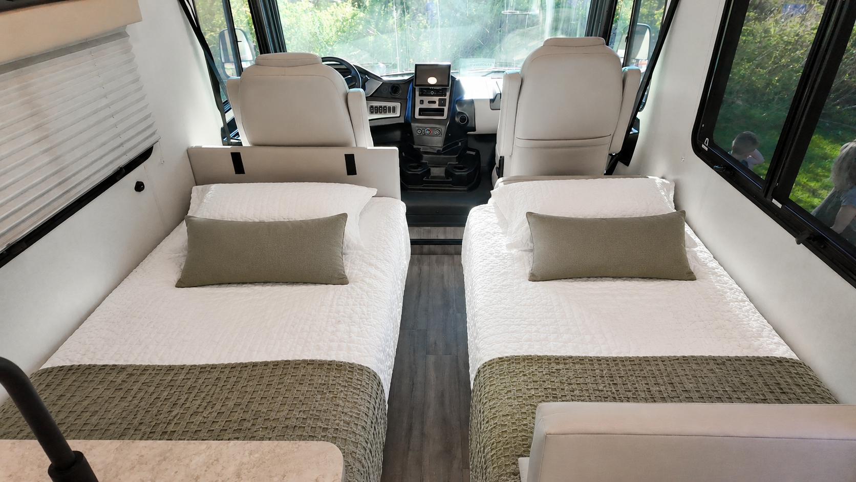 Two single beds inside a camper van with pillows, bedding, and front driver seats visible.