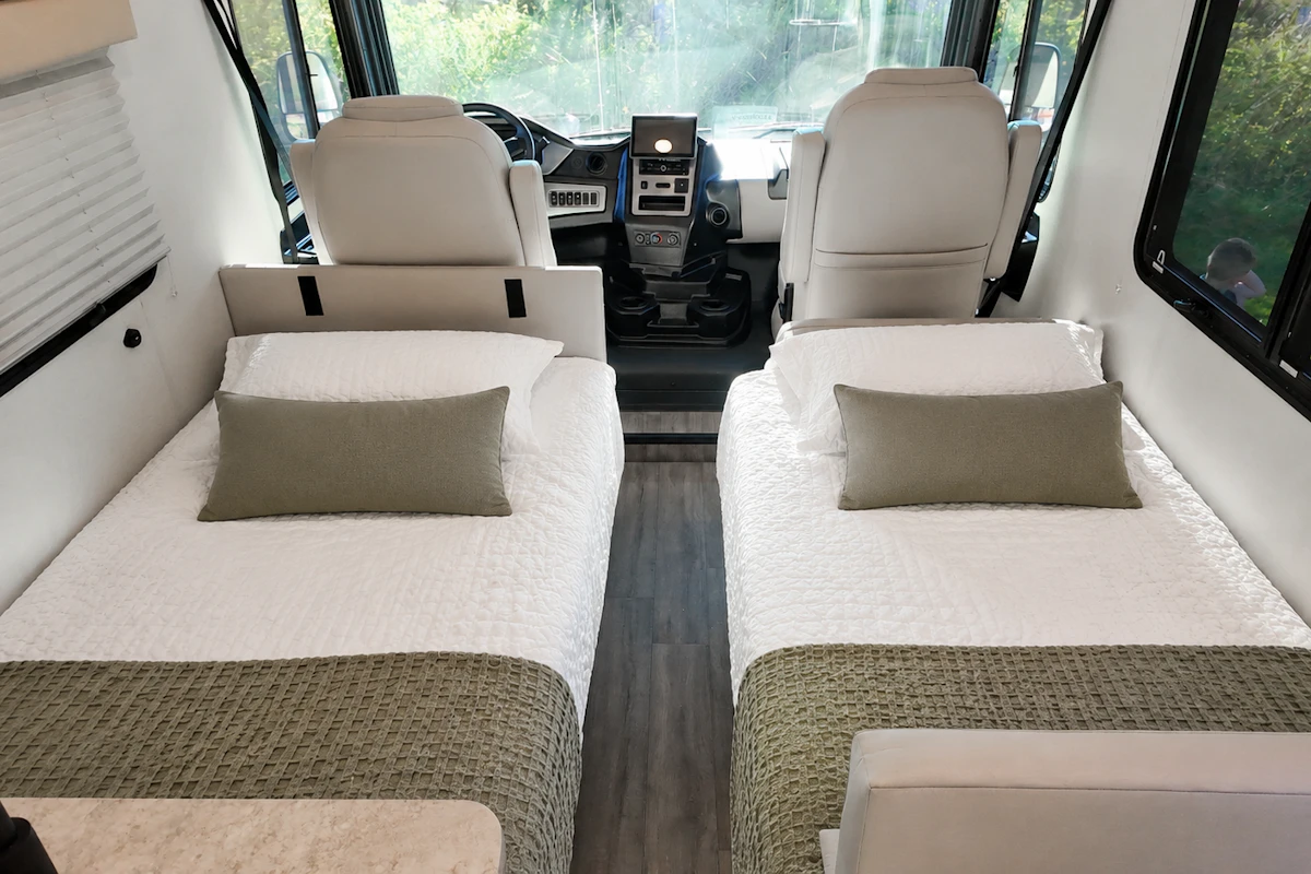 Two single beds inside a camper van with pillows, bedding, and front driver seats visible.