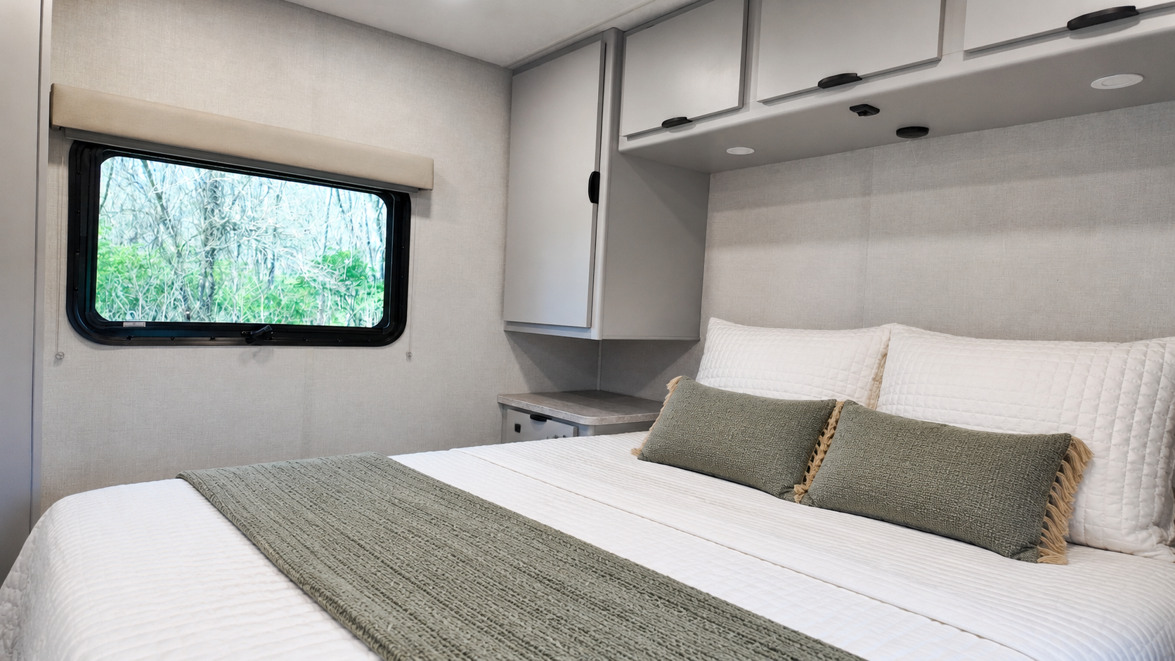 Van interior with bed, overhead storage cabinets, side cabinets, window, and pillows neatly arranged on the bed.