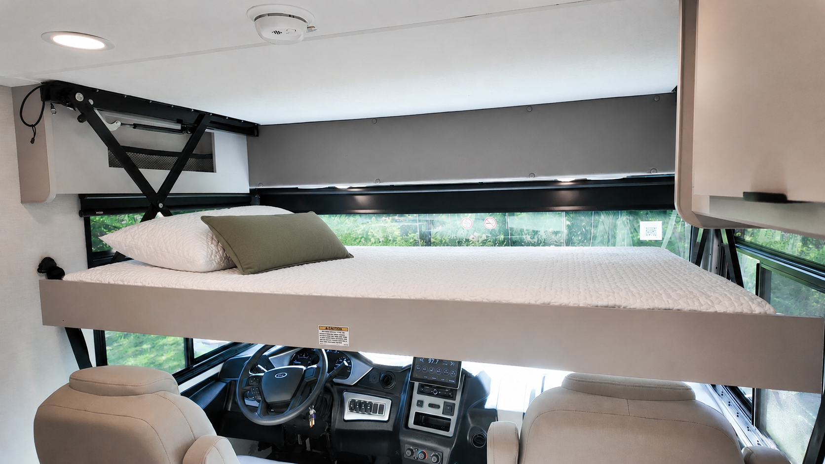 Over-cab bed above cockpit with mattress, pillow, and blanket in camper van interior.