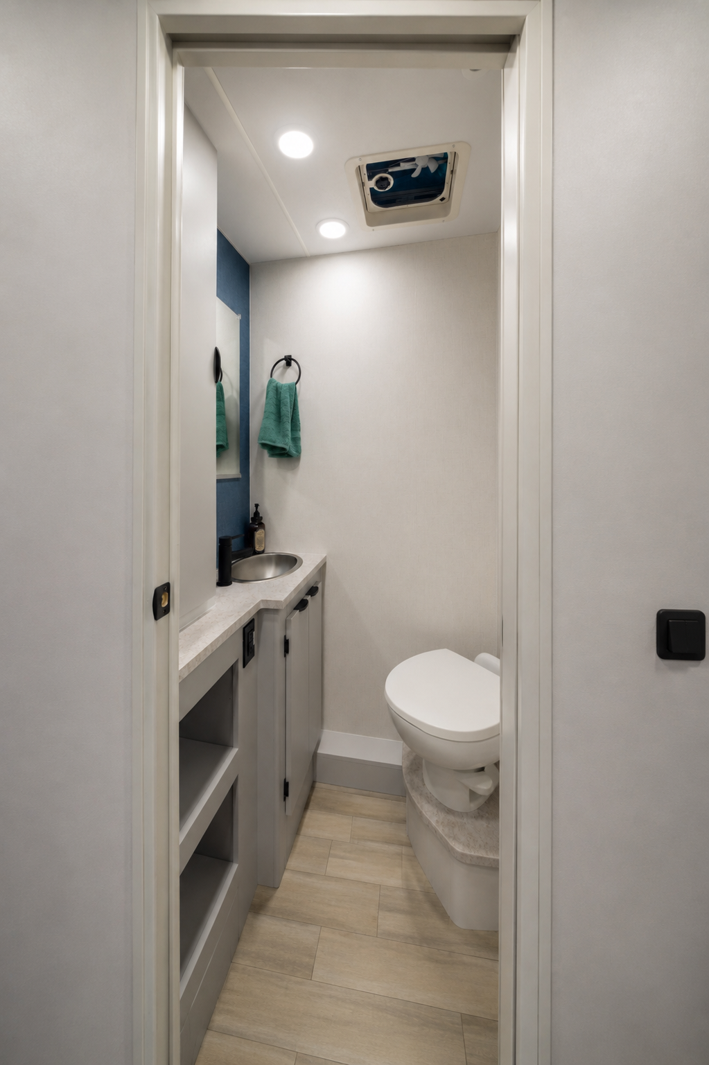 Van bathroom interior with toilet, small sink, countertop, storage cabinets, and two towels hanging on the wall.