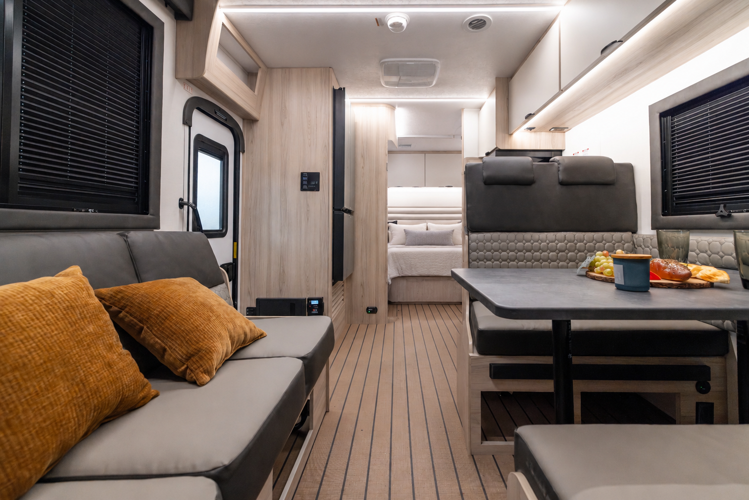 Van interior with seating area, dining table, kitchen, and visible bed in the rear, modern design.