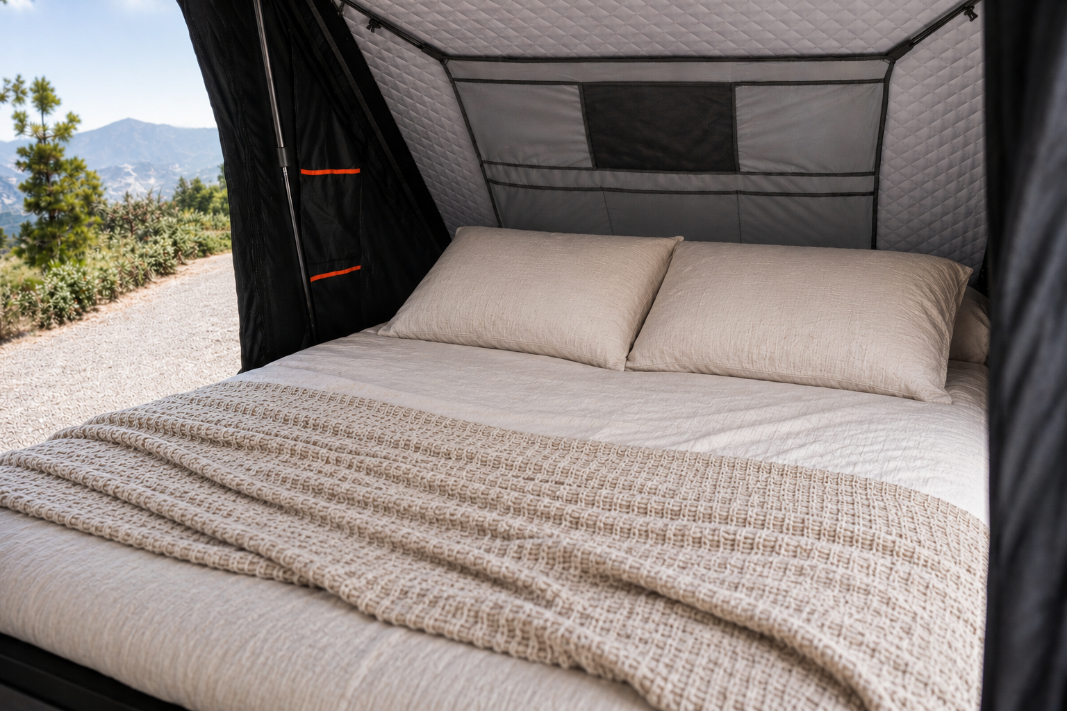 Van interior with a double bed, two pillows, window, and textured blanket inside a raised roof tent.