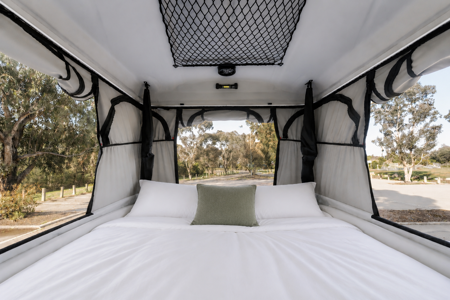 Van interior with raised roof, double bed, pillows, netted storage above, surrounded by windows.