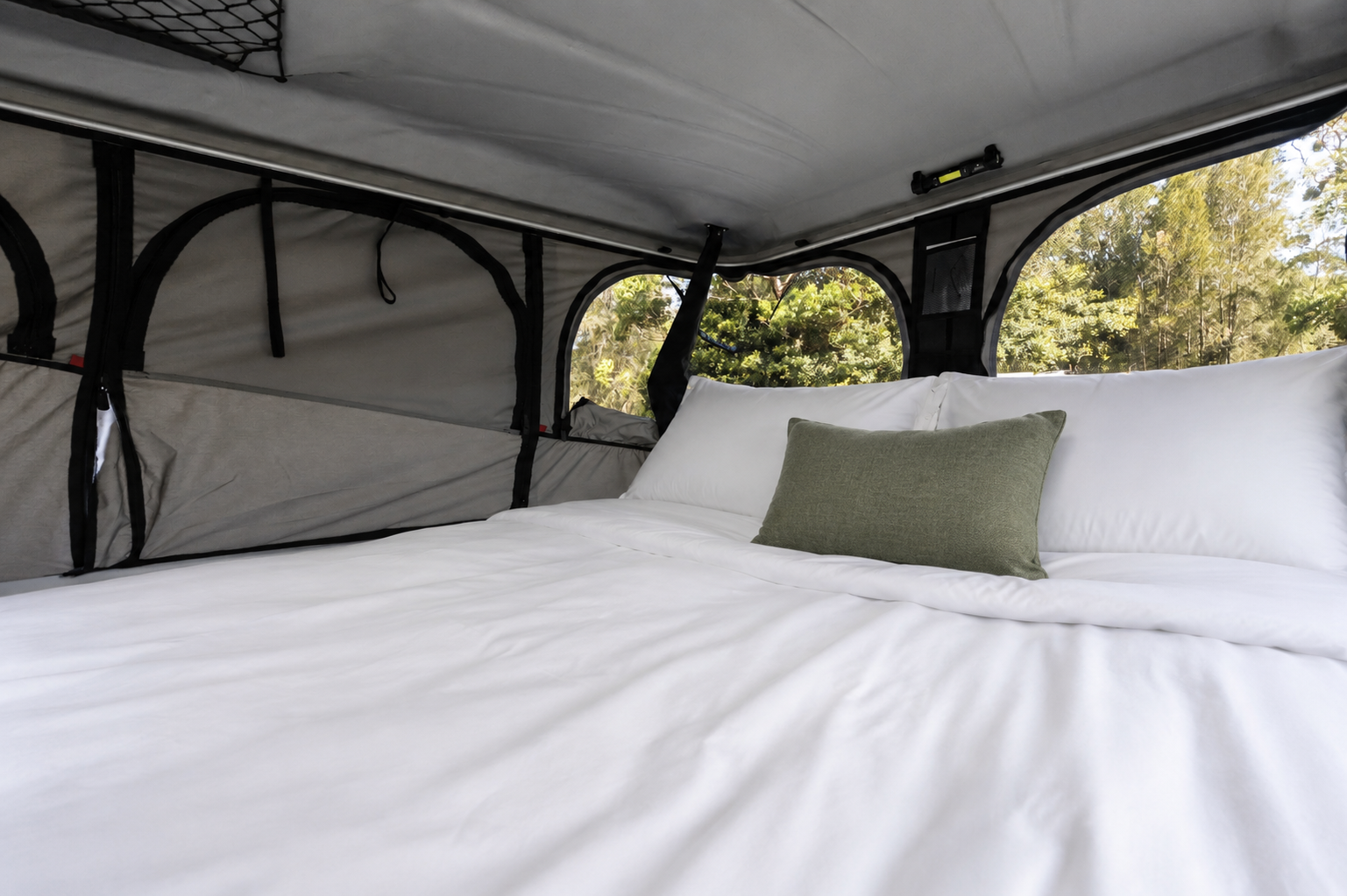 Pop-up roof tent interior with made bed, two pillows, mesh storage, zippered windows, and fabric wall panels.