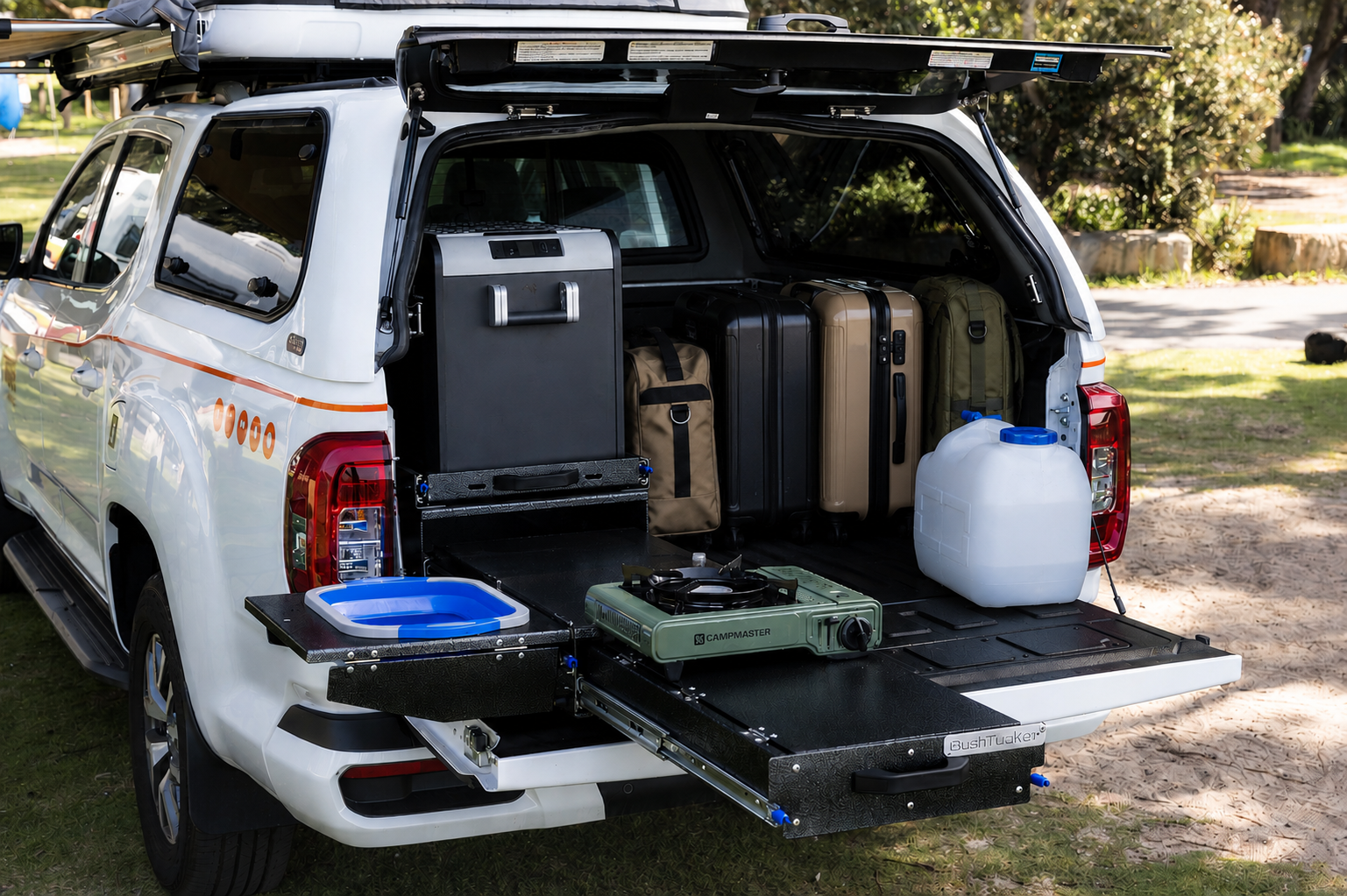 Rear view of medium campervan with open trunk showing kitchen equipment, storage drawers, water container, luggage inside.