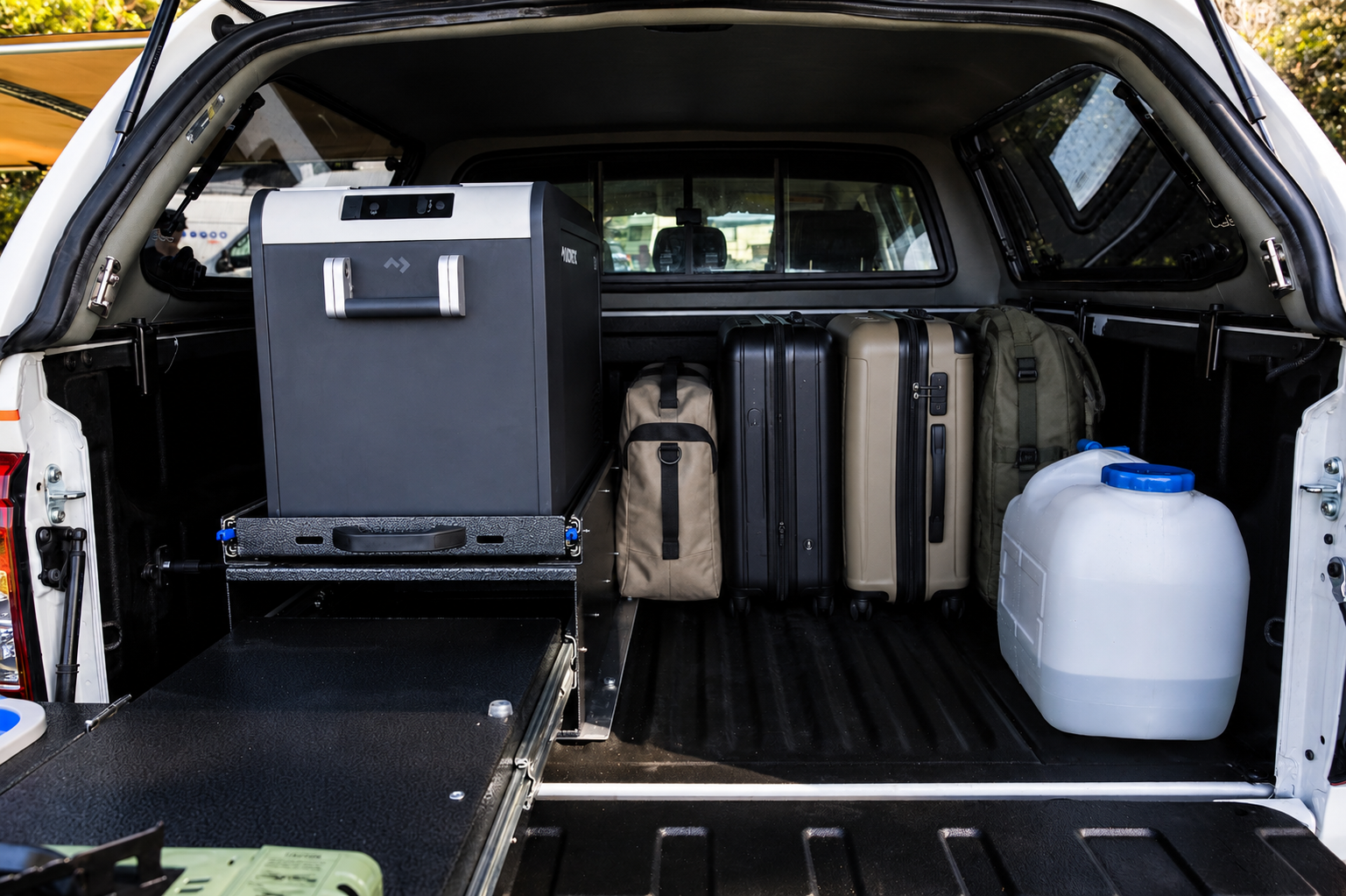 Rear view of van interior with fridge, suitcases, bags, and water container in storage area.