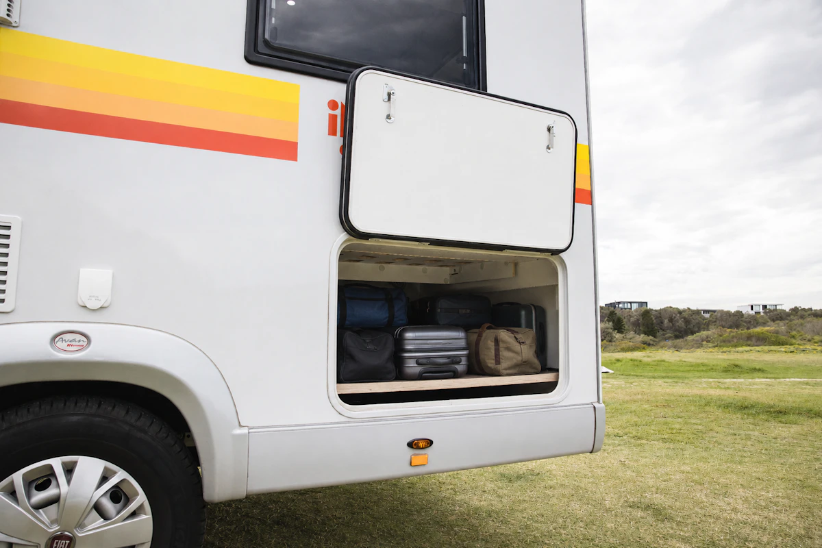 Side view of campervan exterior showing open luggage storage compartment with bags and suitcases inside.