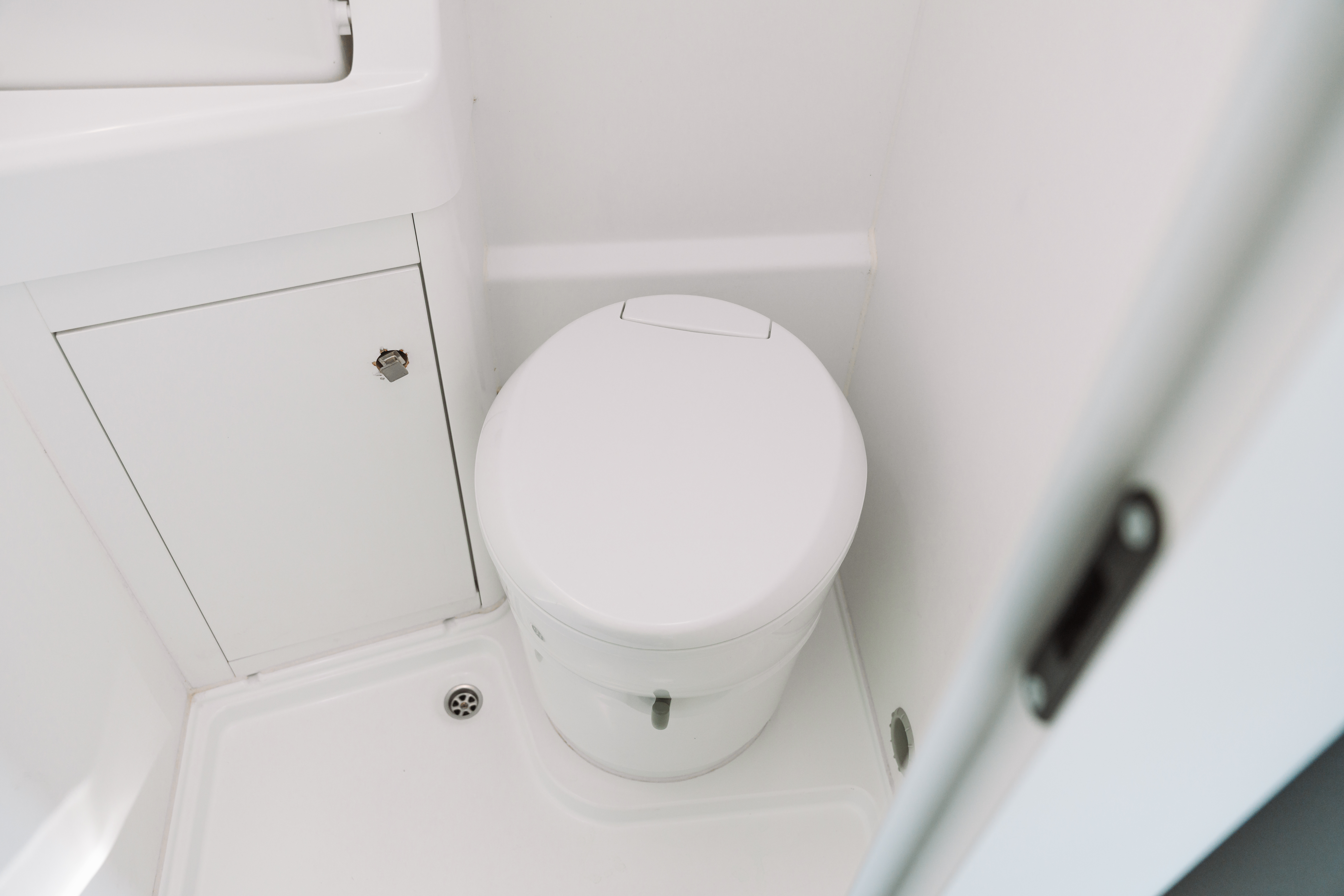 Compact van bathroom with closed toilet, white cabinet, and shower floor visible.