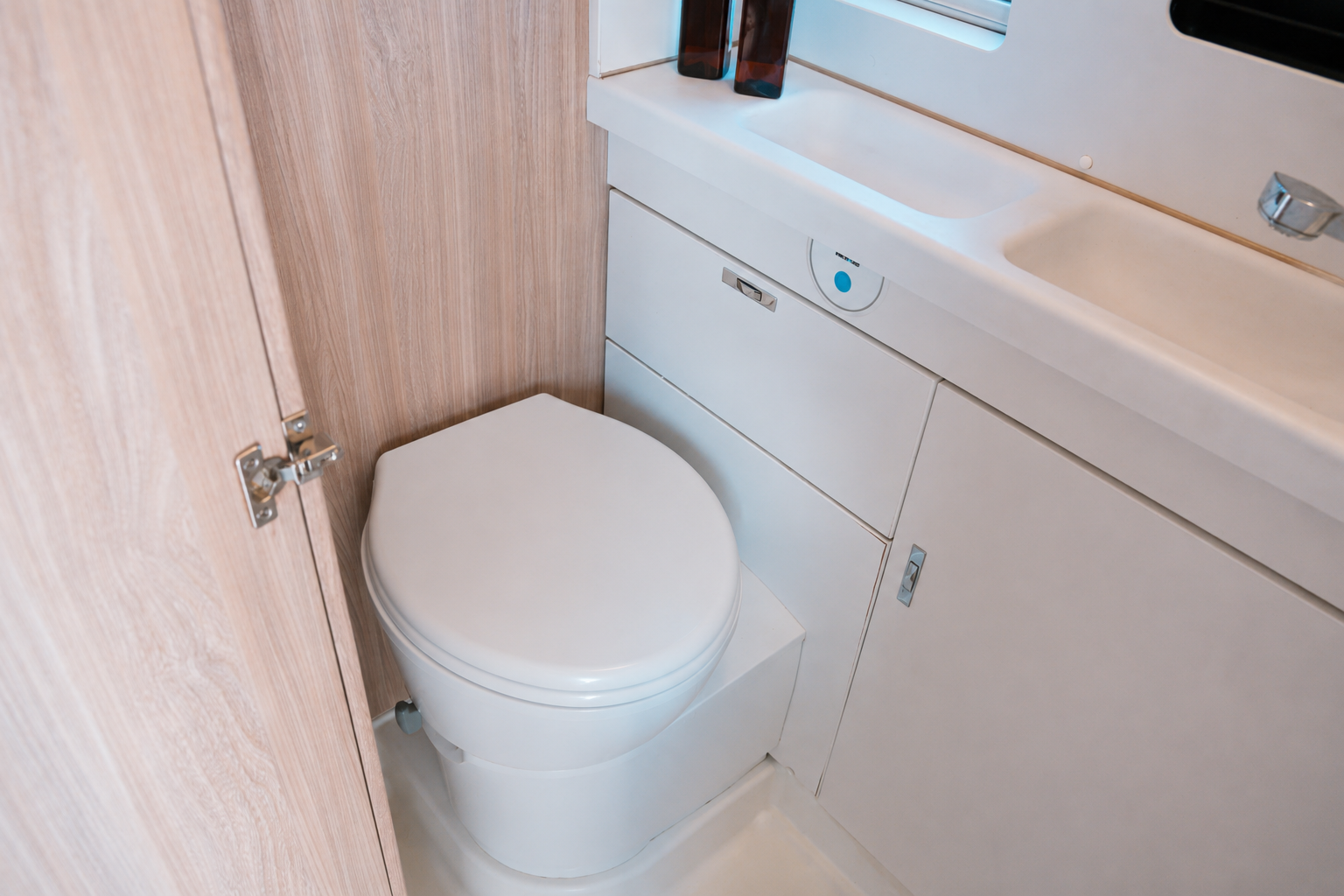 Compact van bathroom with toilet, built-in sink, and storage cabinets, viewed from above near the door.