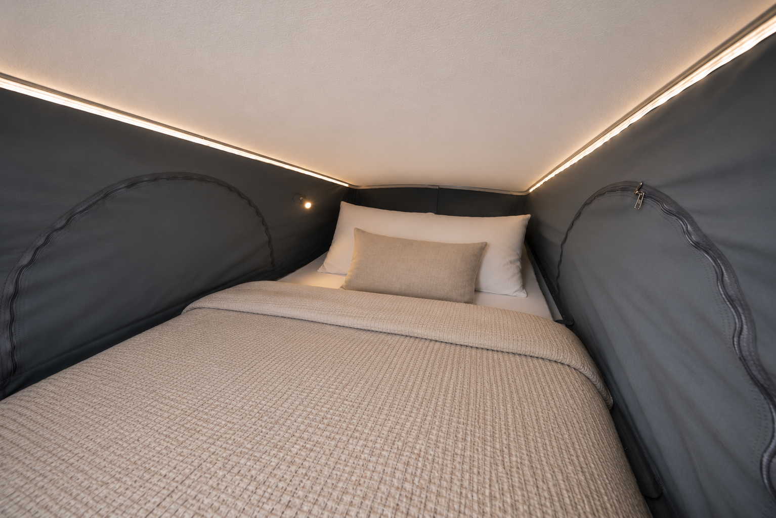 Interior van view showing bed with beige blanket and pillows under a pop-up roof tent with LED lighting.