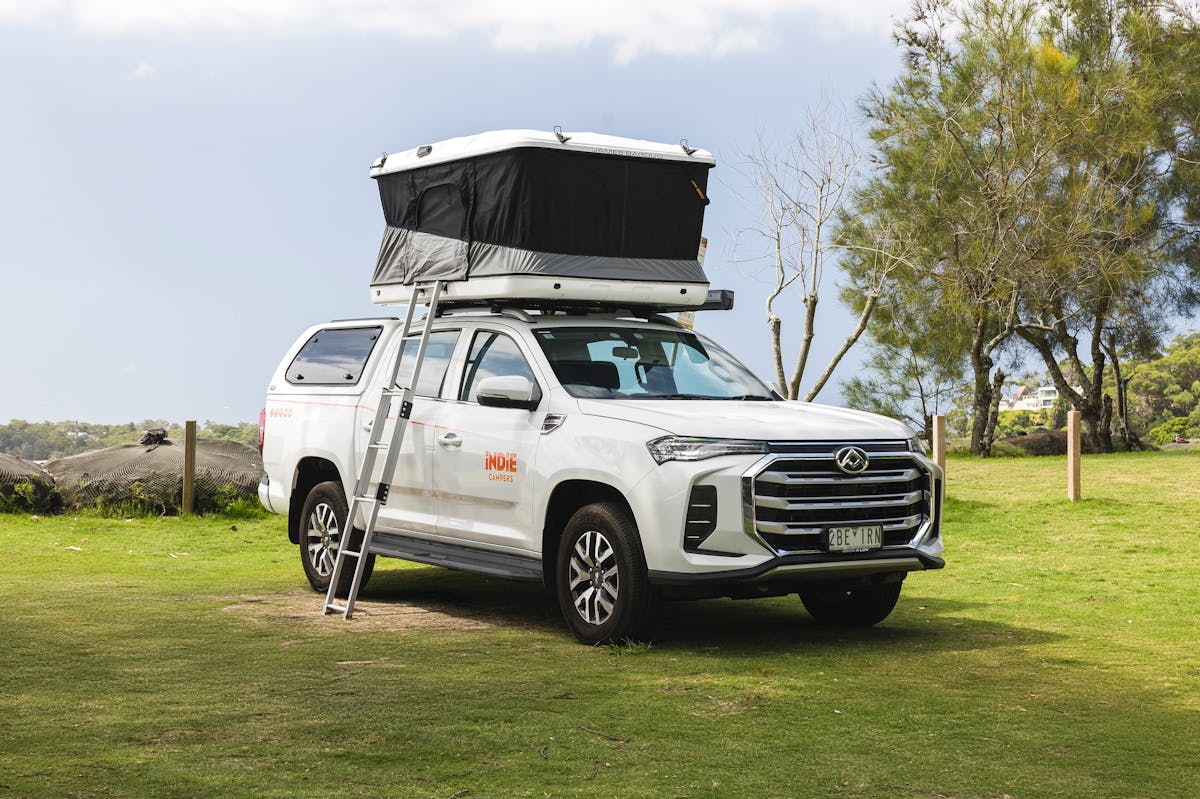 Front-side view of a medium campervan with a roof tent and exterior ladder.
