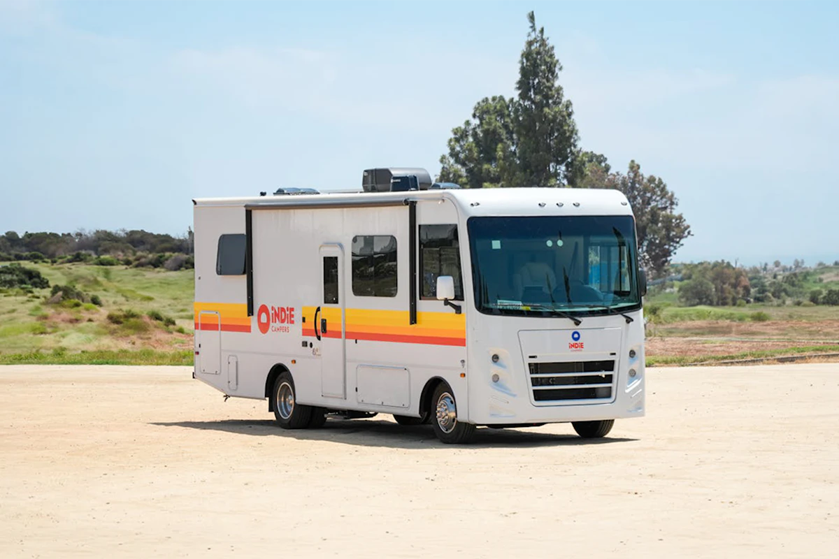 White Indie Campers RV parked outdoors on a sunny day with grass and trees in the background.