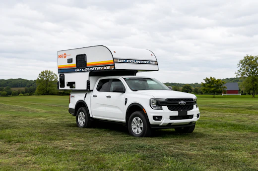 Front side view of medium-sized pickup camper with over-cab sleeping area and compact, box-shaped rear layout.