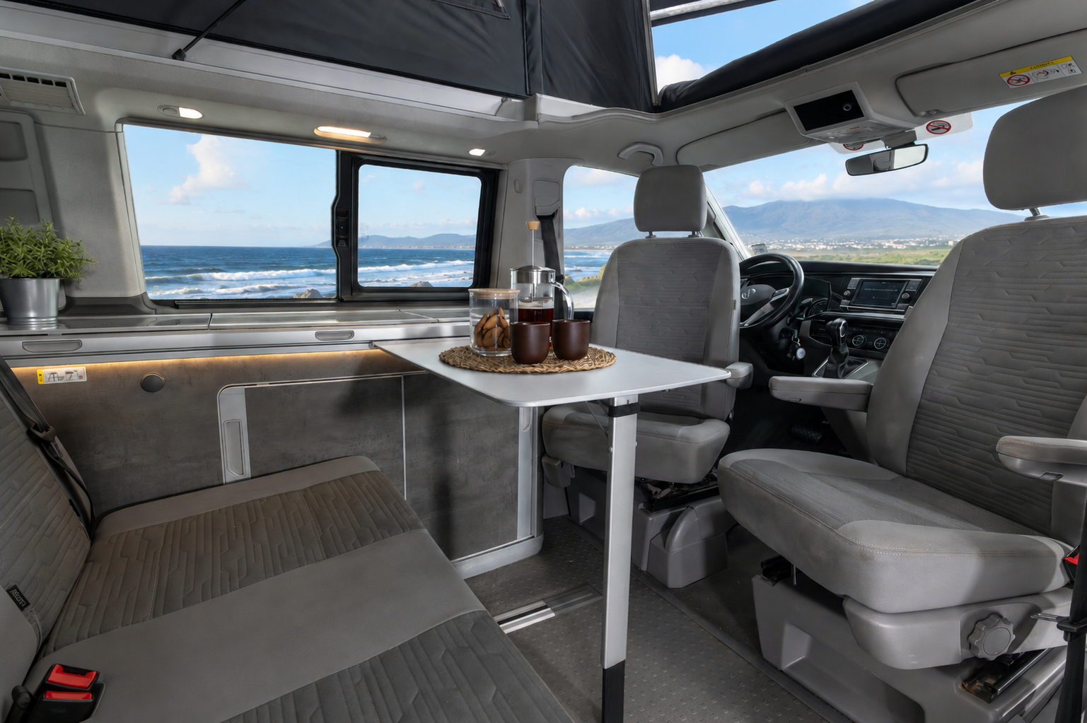 Van interior with front seats, a bench seat, foldable table, small kitchen counter, and window.